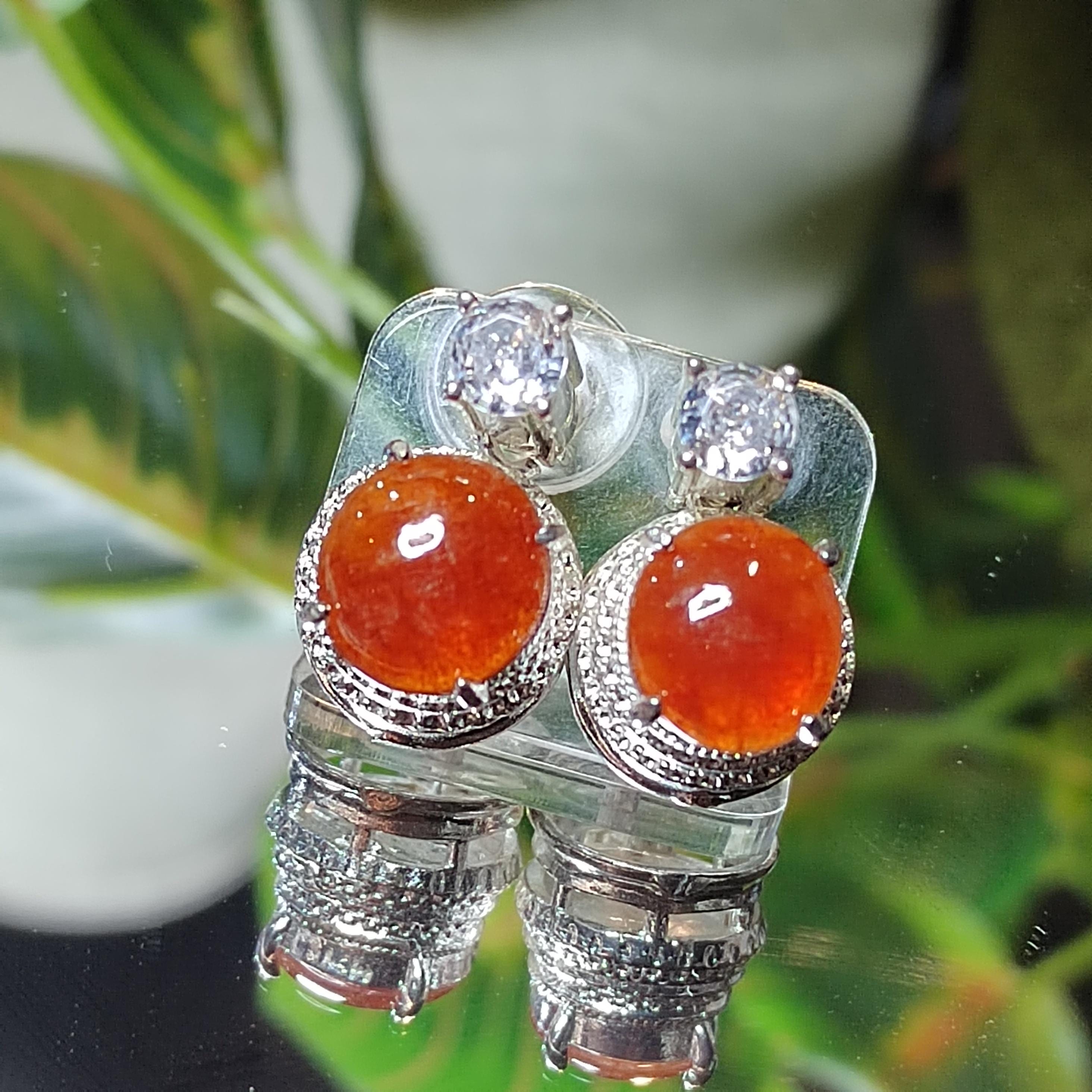 Pair of silver earrings with orange gemstones on a green leafy background