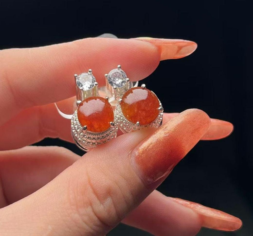 Silver earrings with orange gemstones held between fingers against a black background