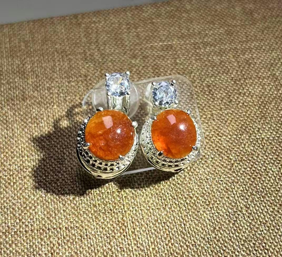 Pair of earrings with orange gemstones and silver settings on a textured brown surface