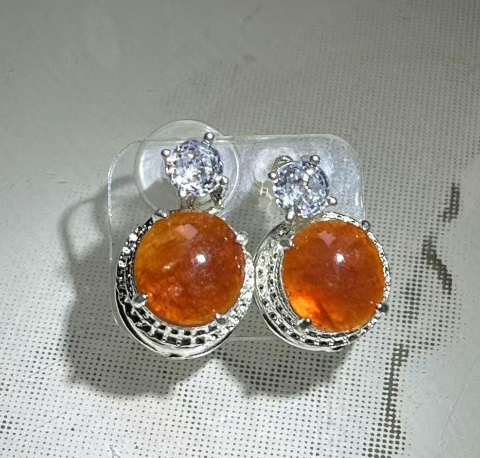 Pair of cabochon orange gemstones and silver settings on a textured surface