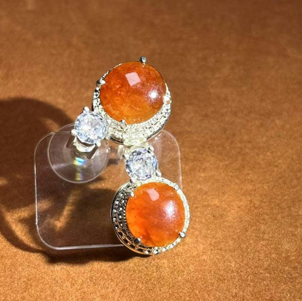 Pair of earrings with orange stones and clear gemstones on a brown background