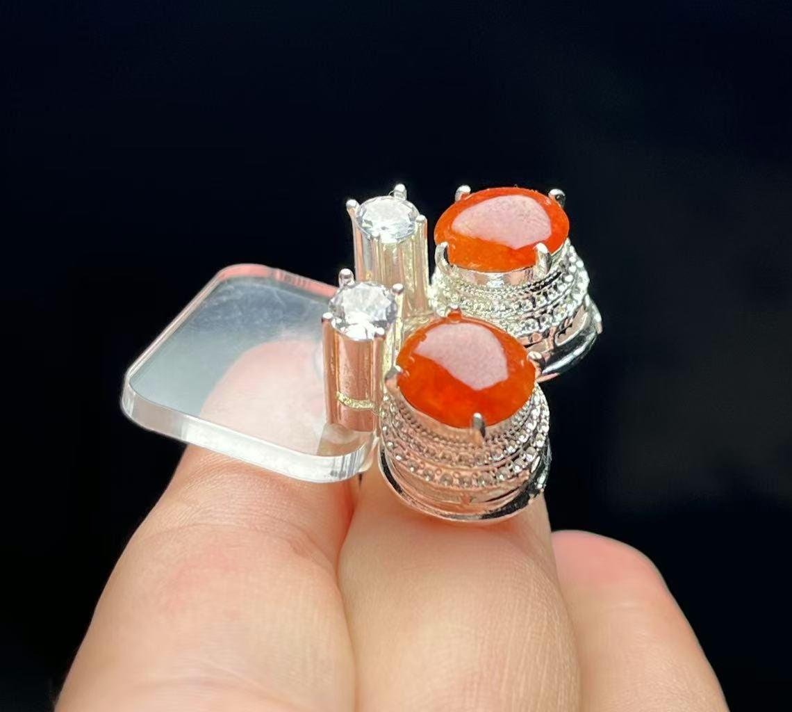 Two silver rings with orange gemstones held between fingers against a dark background