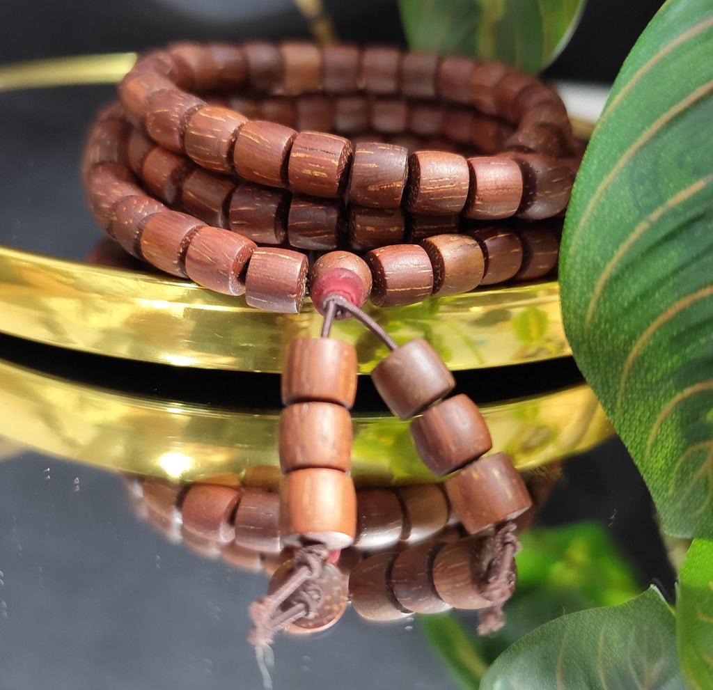 Wooden beaded bracelet on a reflective surface with green leaves in the background