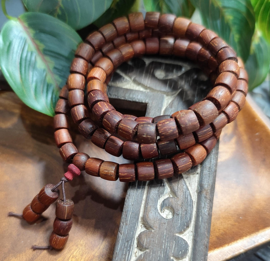 Wooden beaded bracelet on a decorative wooden stand with green leaves in the background