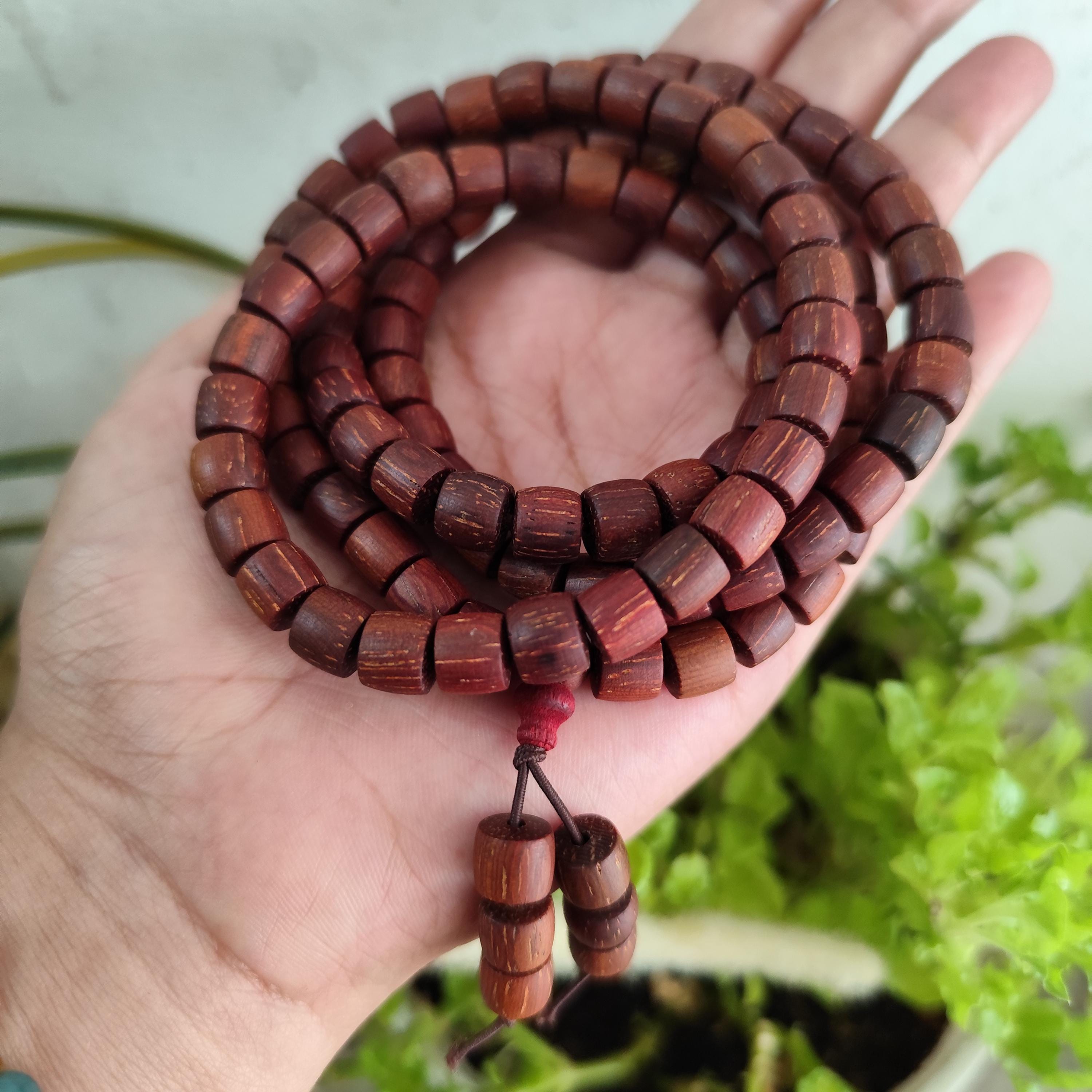 Wooden prayer beads held in a hand with a blurred green background