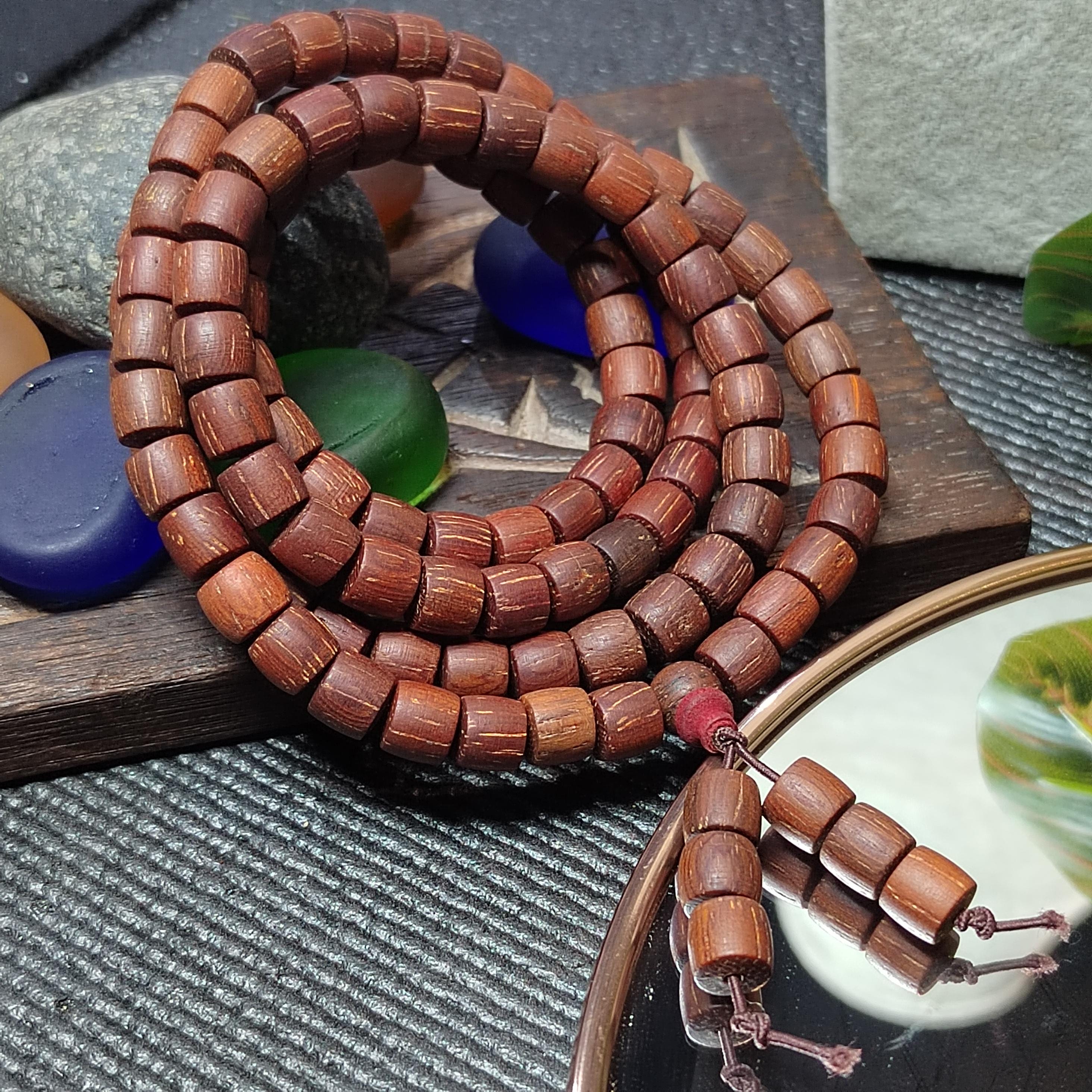 Wooden beaded bracelet on a textured surface with pebbles and a leaf.