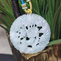 Carved jade pendant on a gold chain against a green plant background