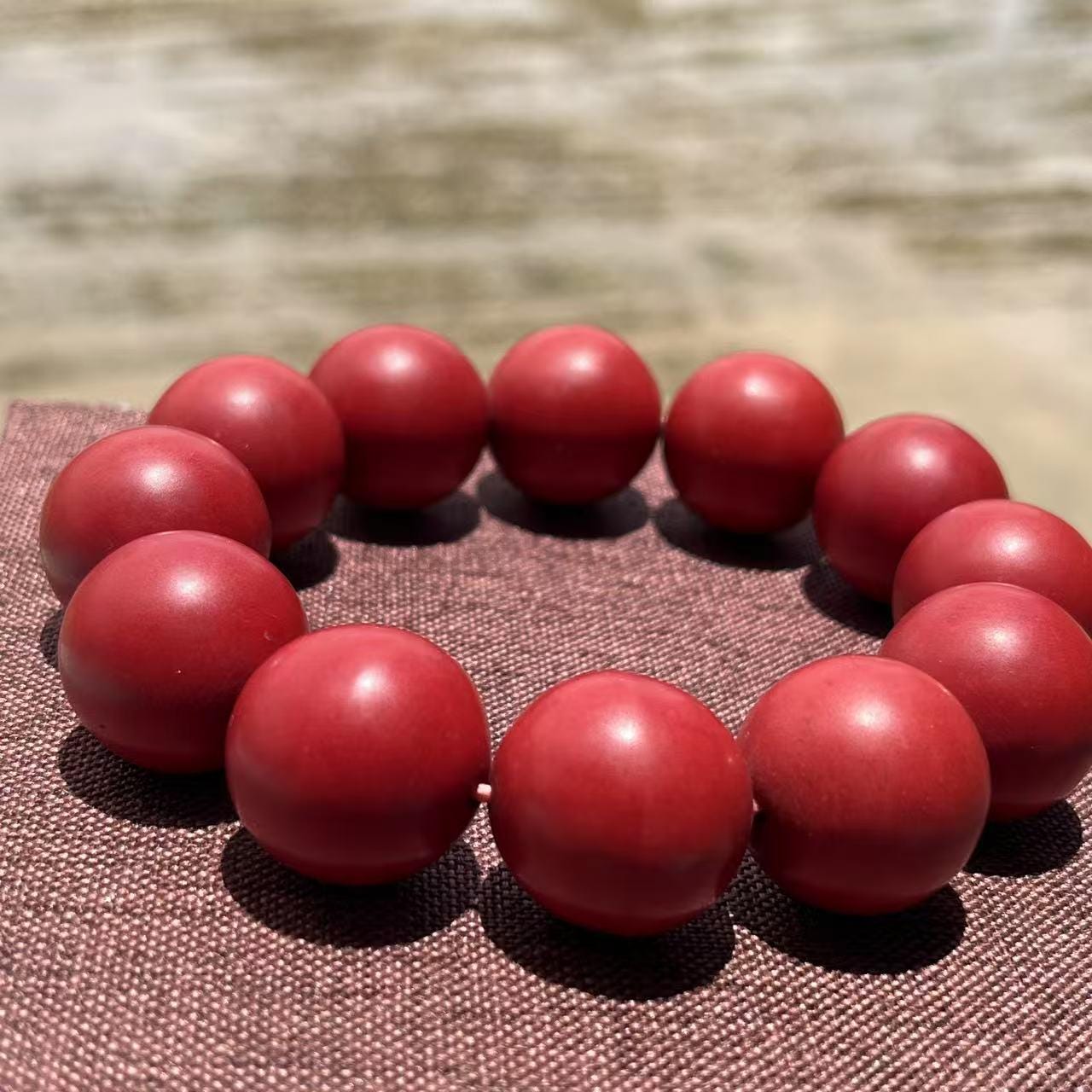 Red beaded bracelet on a textured surface with a blurred natural background