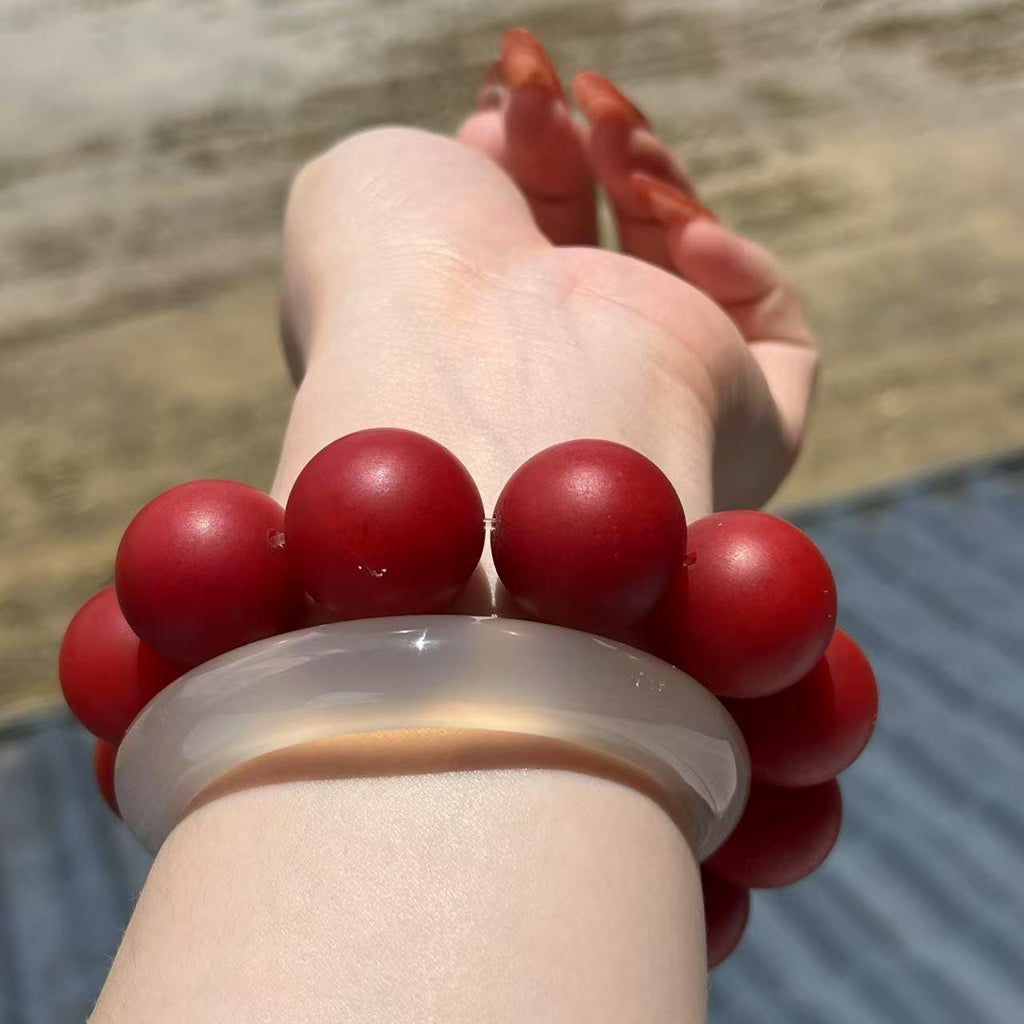Hand wearing a red beaded bracelet with a clear stone on a blurred natural background