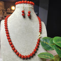 Red beaded necklace and earrings on a gray mannequin with a blurred indoor background