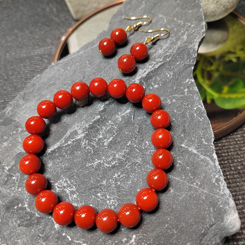 Red beaded bracelet and earrings on a gray stone surface