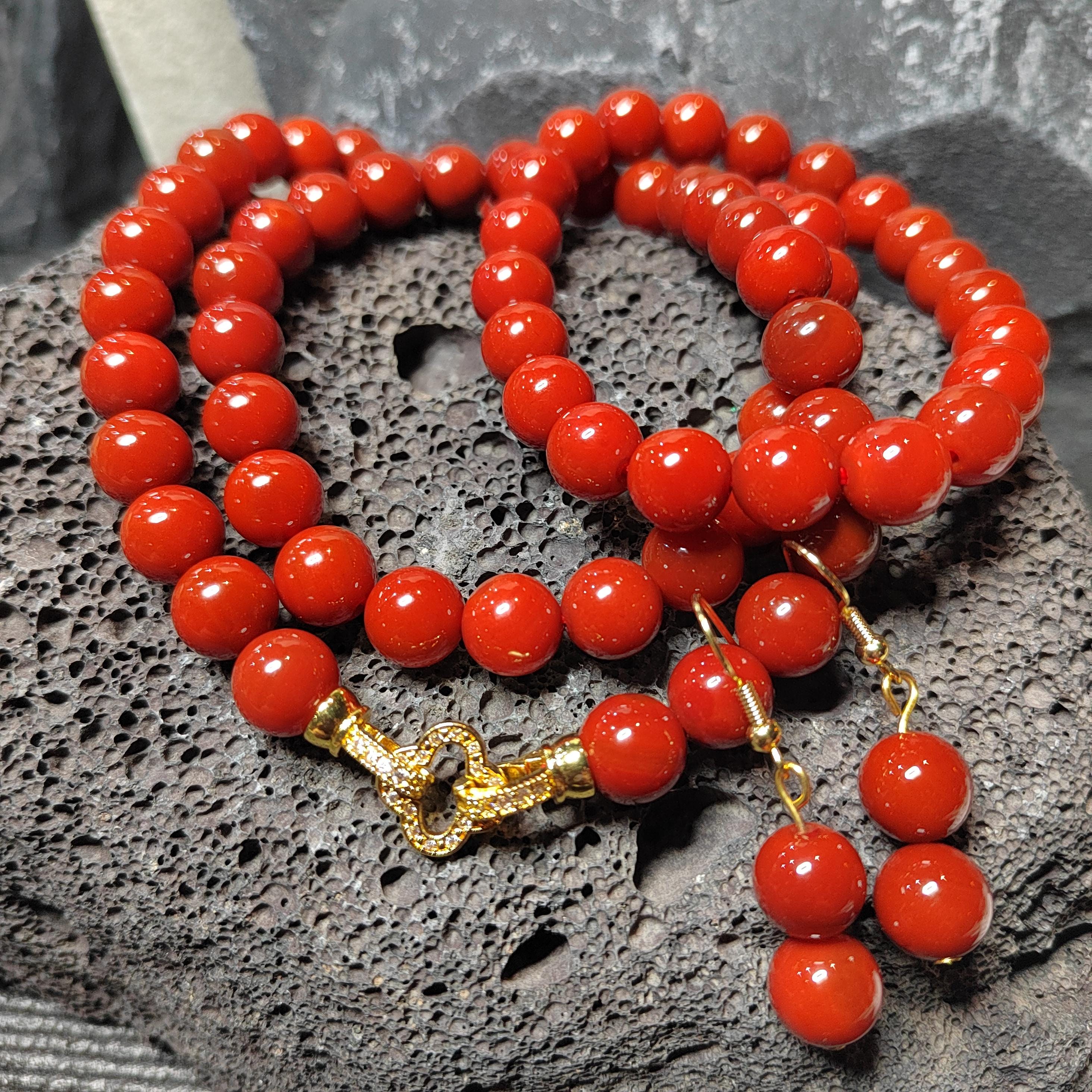Red beaded necklace with a gold clasp on a textured gray surface