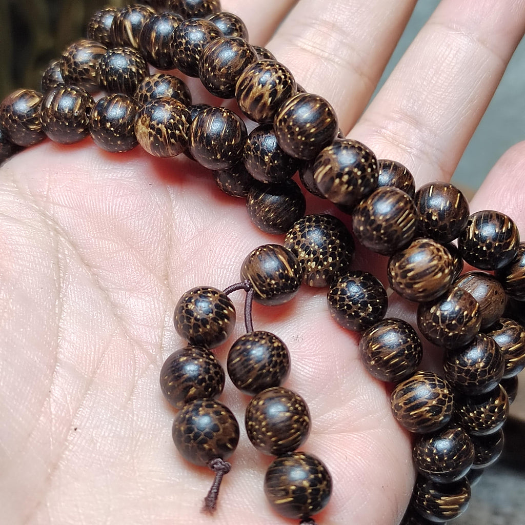 Close-up of a hand holding a string of dark brown beaded rosary.
