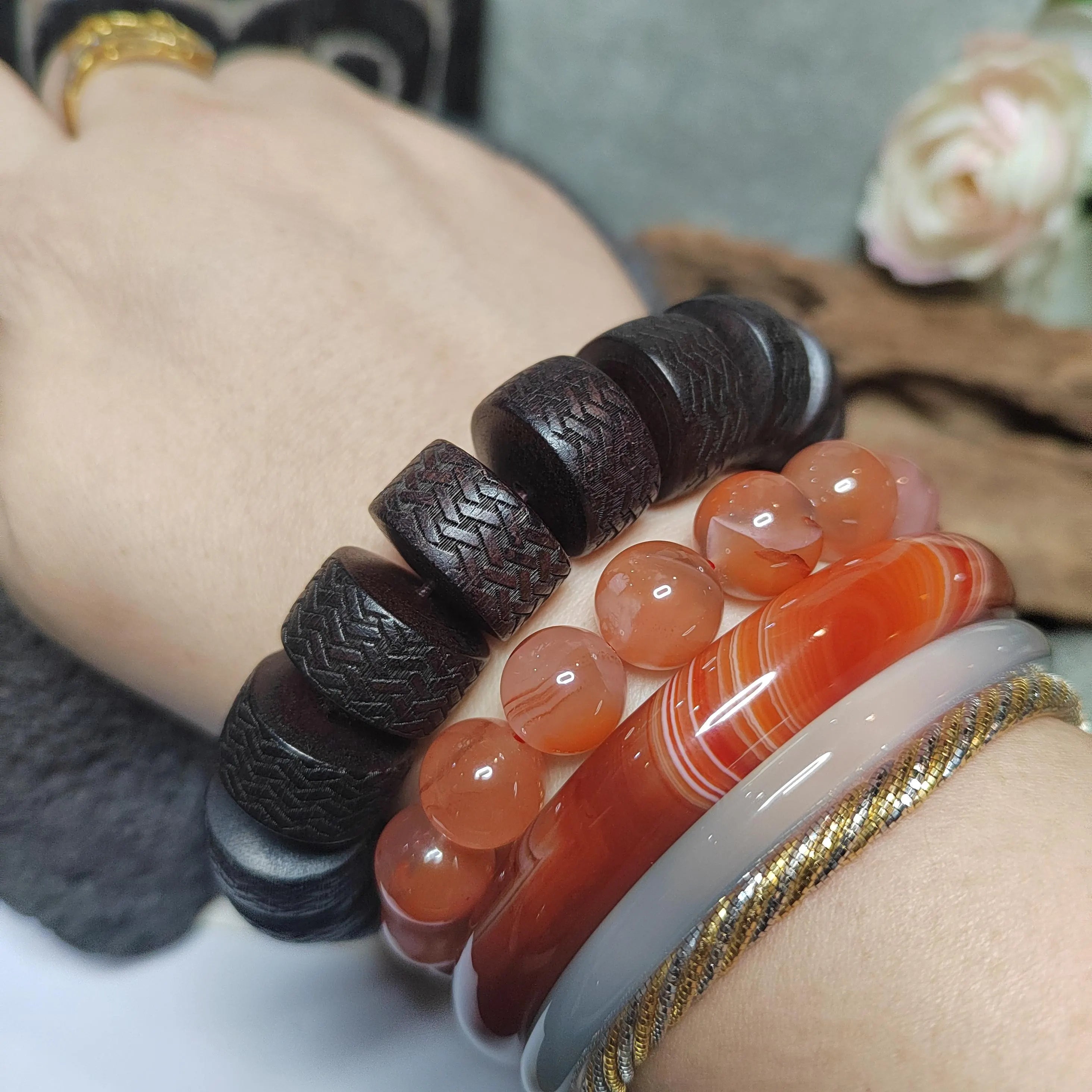 Close-up of hands wearing multiple bracelets with different designs on a neutral background.