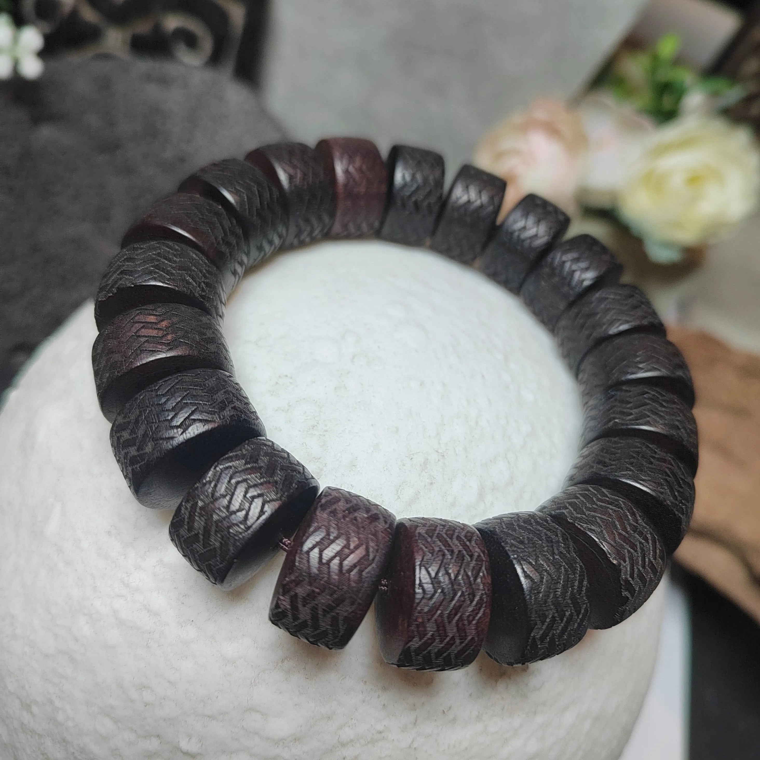 Dark brown beaded bracelet on a white surface with a blurred background