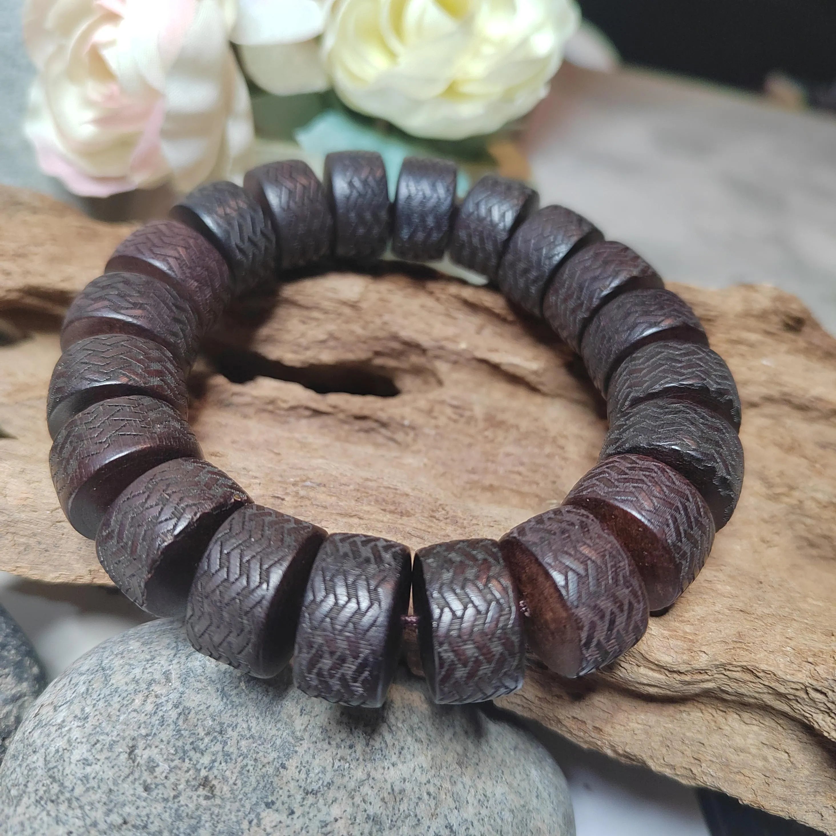 Wooden beaded bracelet on a natural wooden surface with flowers in the background