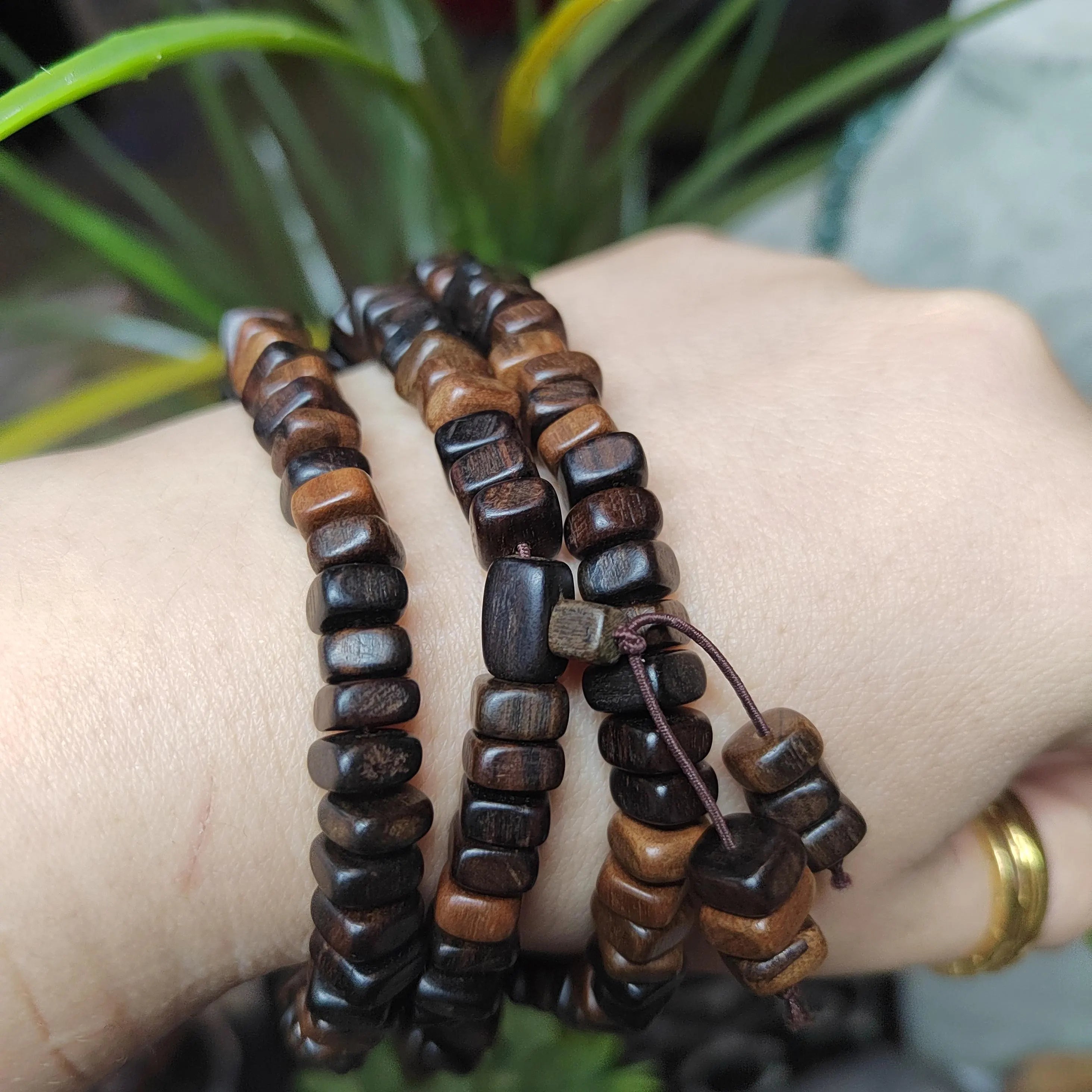 Wooden beaded bracelets on a wrist with a blurred plant background
