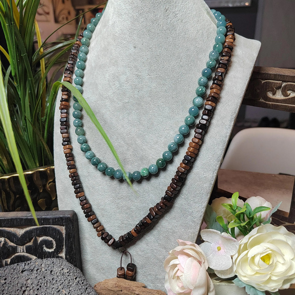 Necklace with turquoise and brown beads on a gray stand with flowers and plants in the background