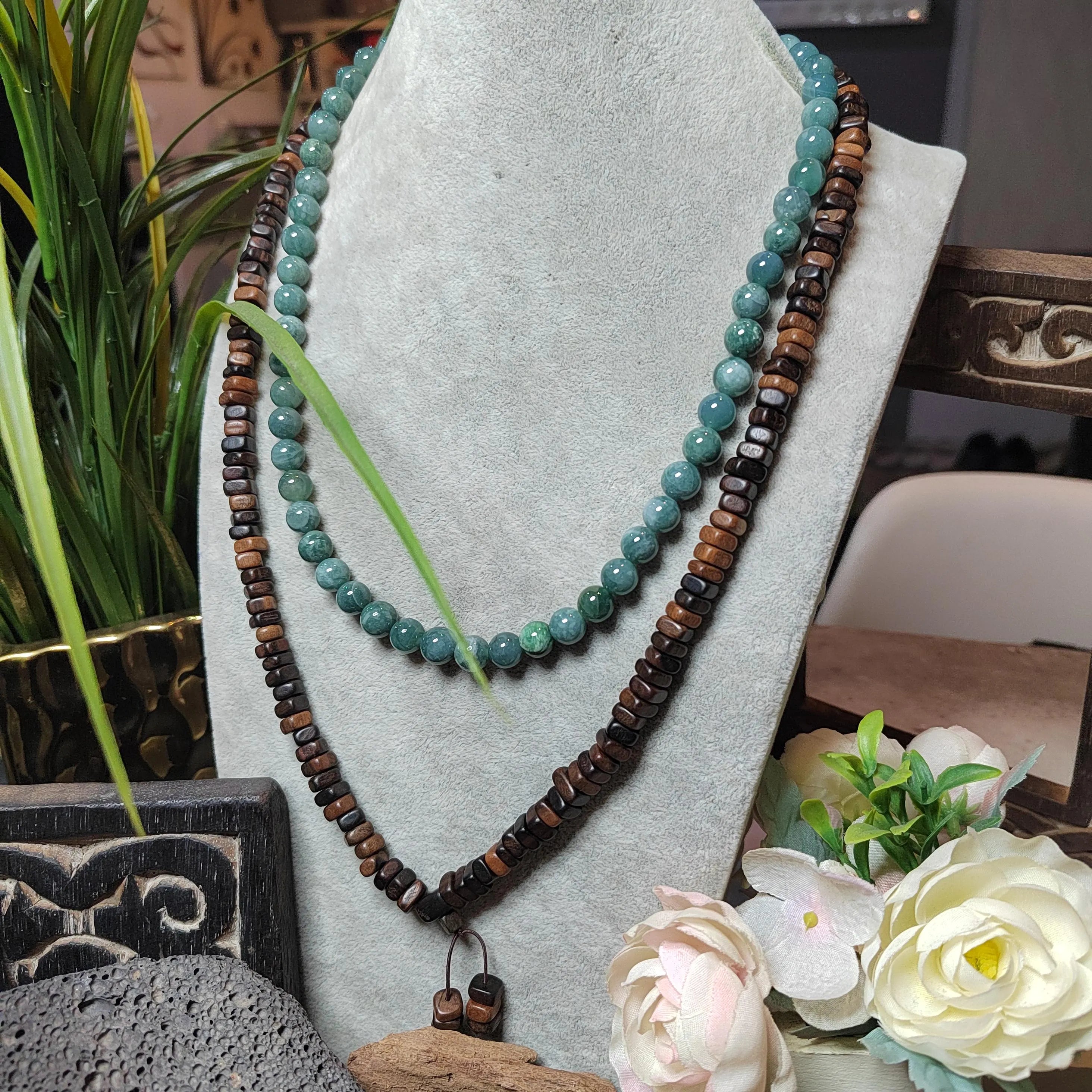Necklace with turquoise and brown beads on a gray stand with flowers and plants in the background