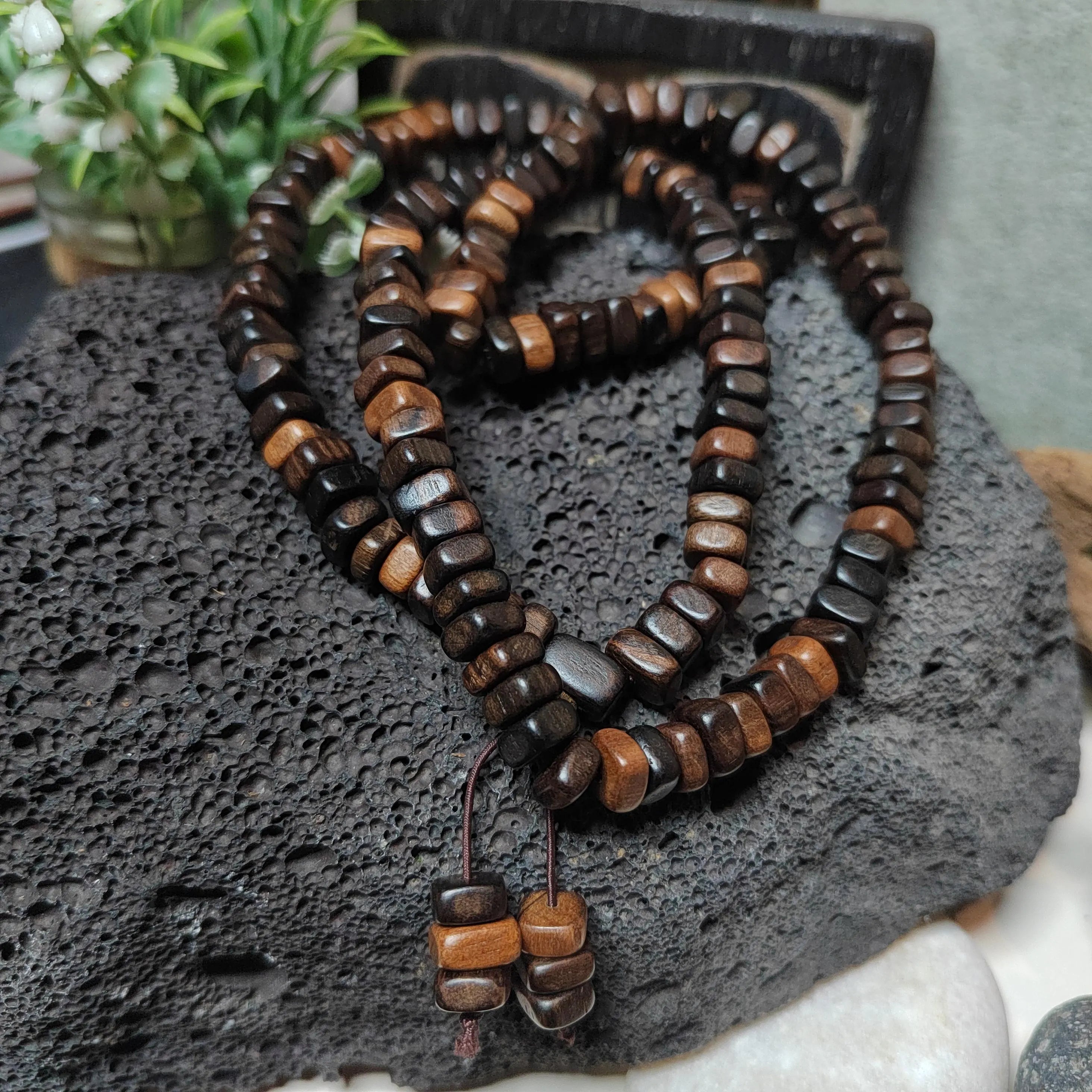 Wooden beaded necklace on a textured surface with a plant in the background