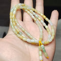 Necklace with green and yellow beads held in a hand against a blurred background