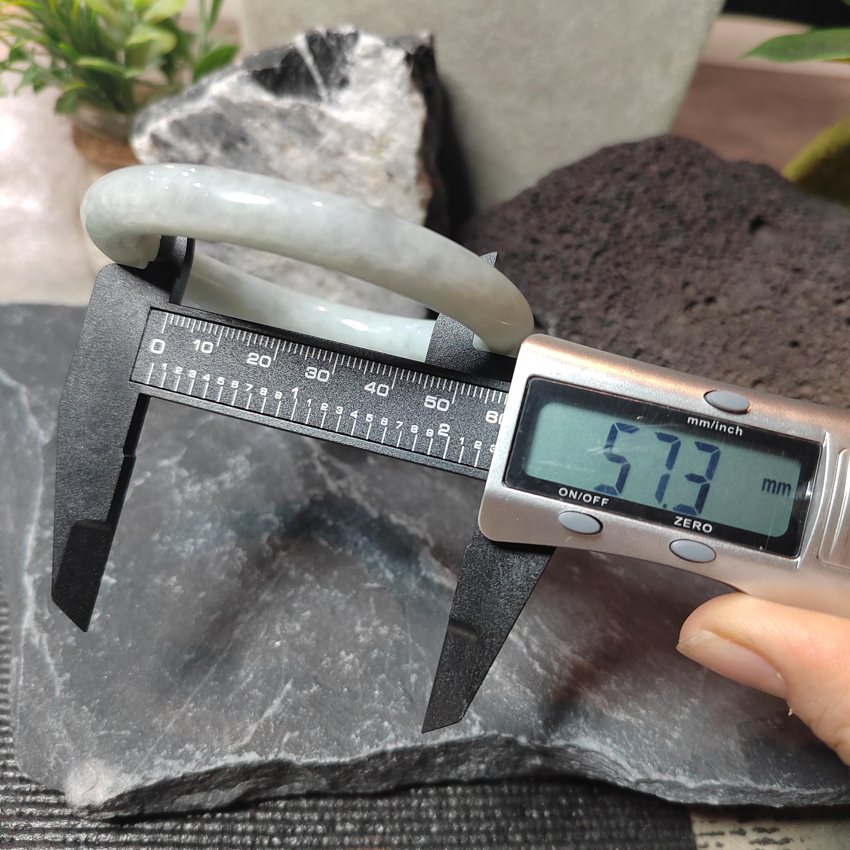 Digital caliper measuring a jade bracelet on a stone surface