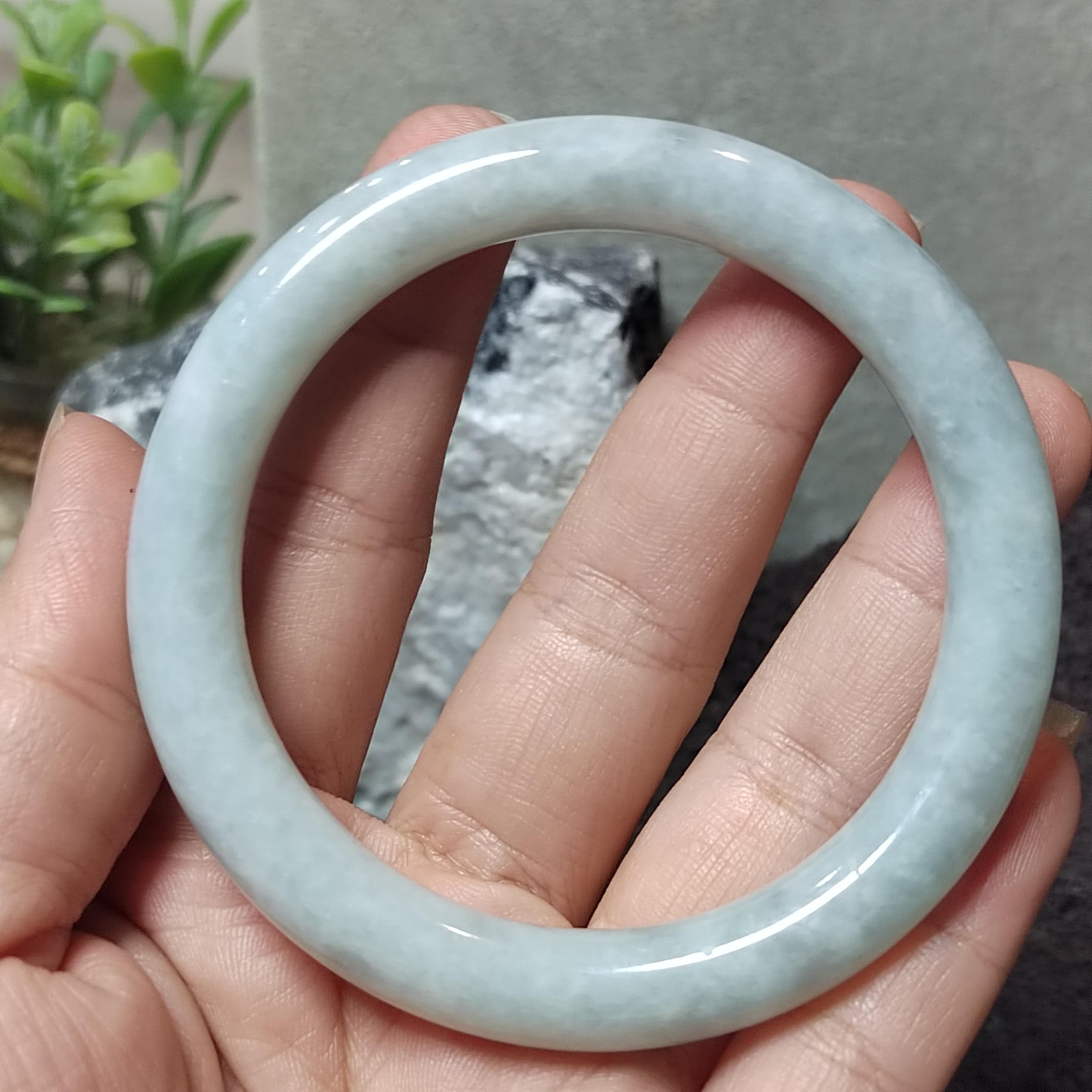 Light blue jade bracelet held in a hand with a blurred background