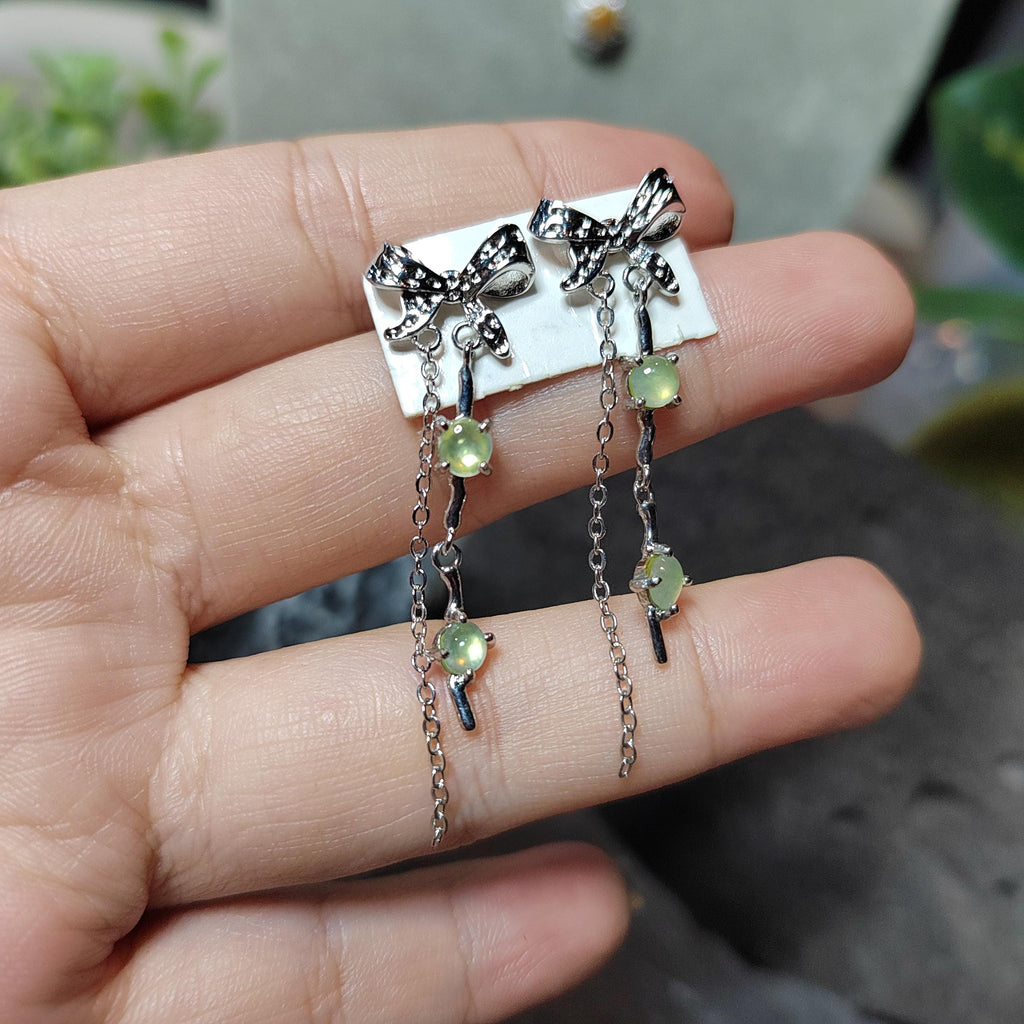Silver earrings with green gemstones held between fingers against a blurred background