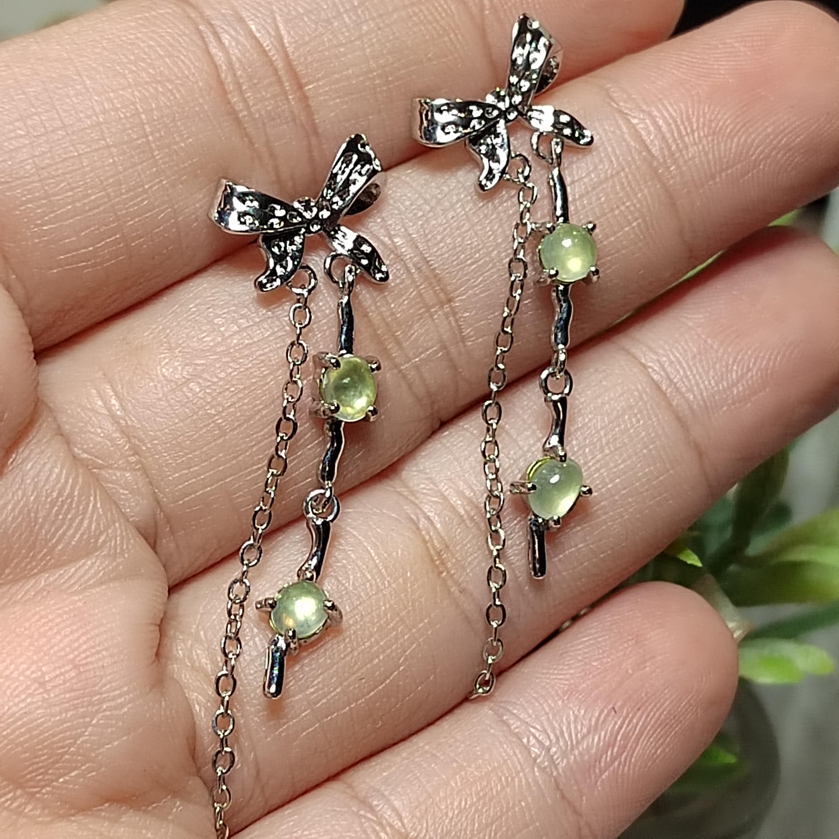 Silver bow earrings with green gemstones held between fingers