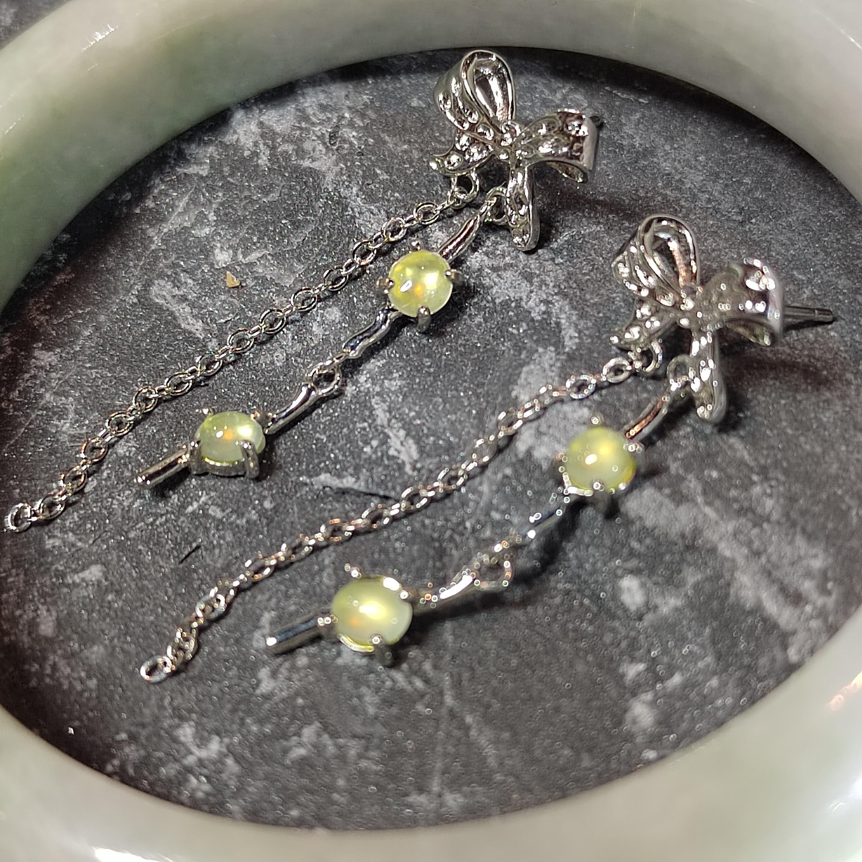 Silver cross earrings with green gemstones on a dark stone surface