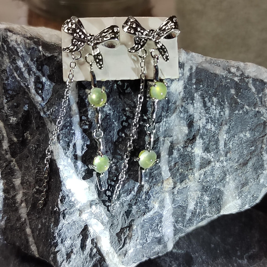 Pair of earrings with bow designs and green beads on a stone surface