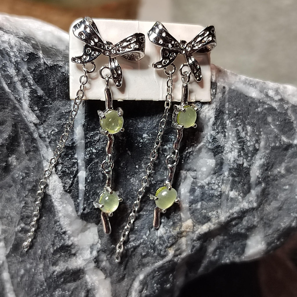 Pair of silver bow earrings with green gemstones on a stone surface