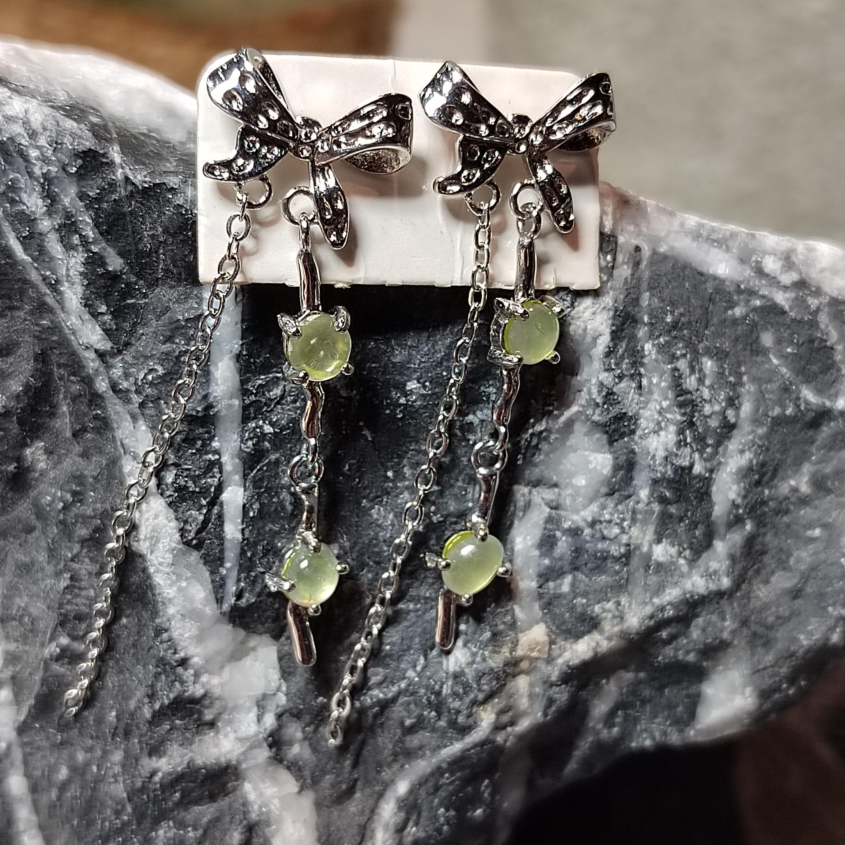 Pair of silver bow earrings with green gemstones on a stone surface