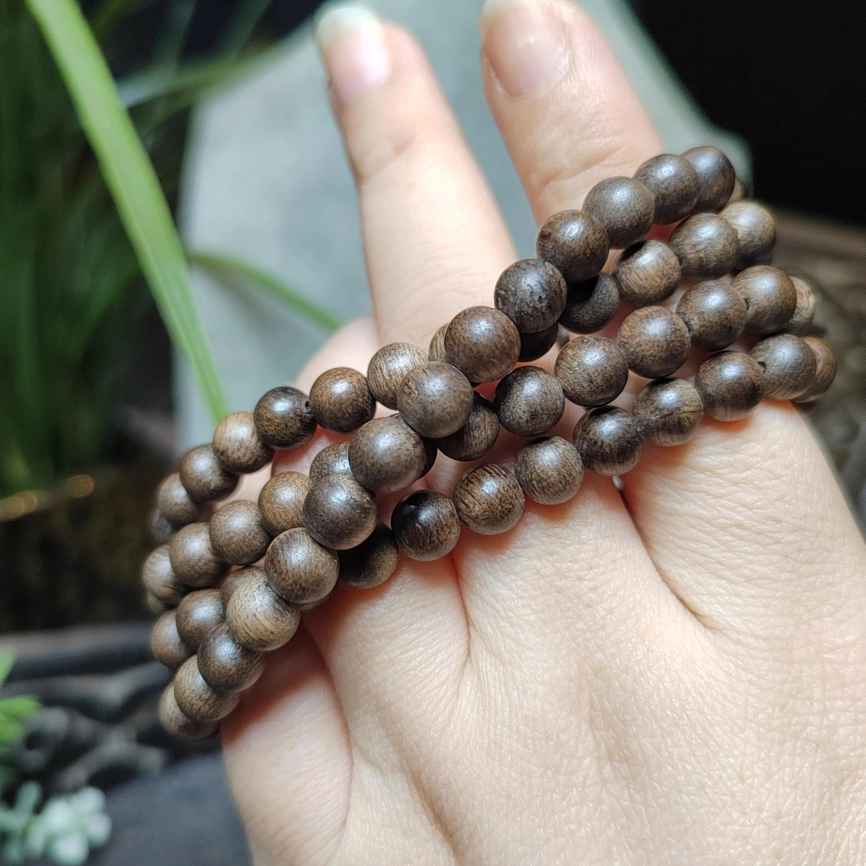 Close-up of a hand holding a stack of brown beaded bracelets with a blurred background.