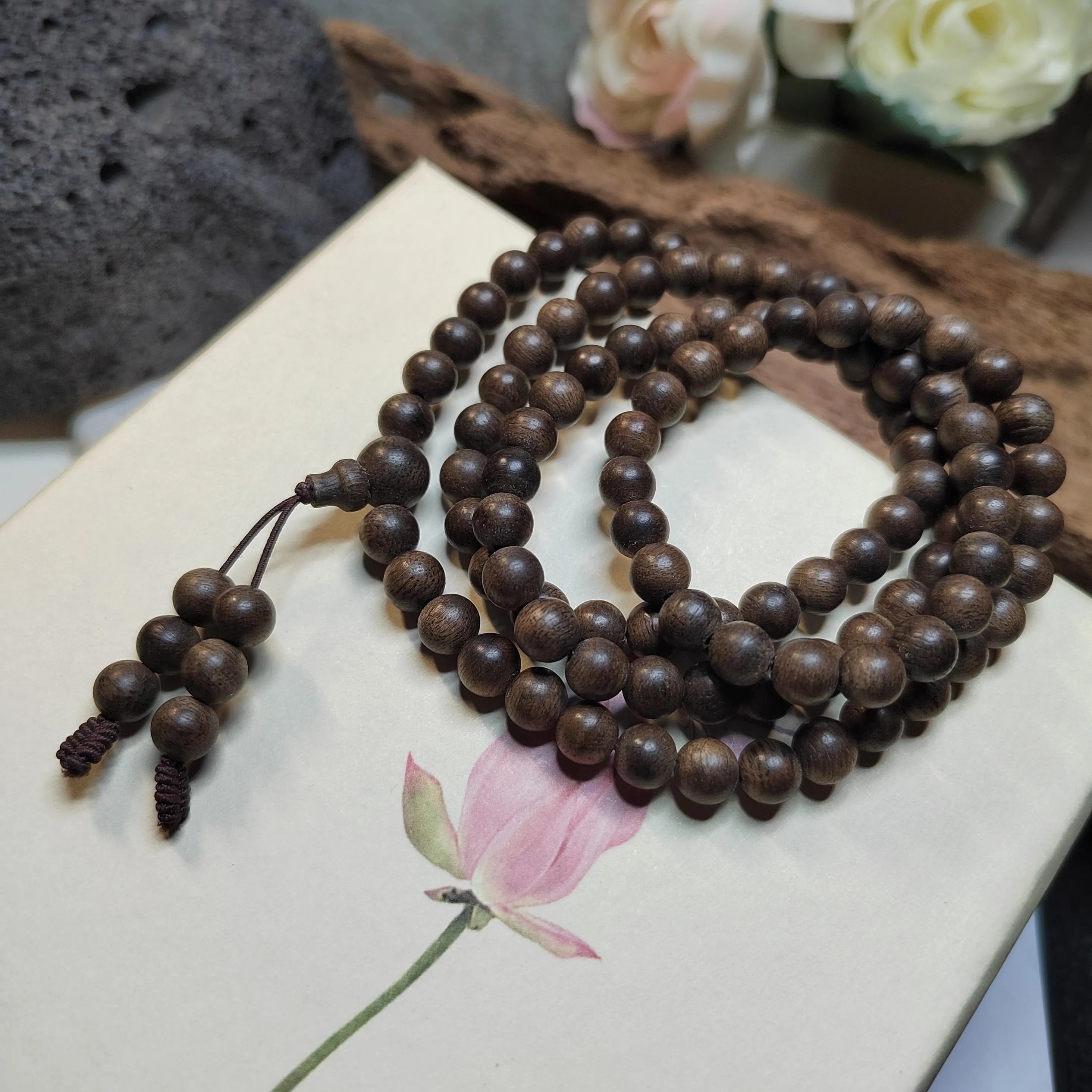 Wooden prayer beads on a floral-patterned surface with flowers in the background