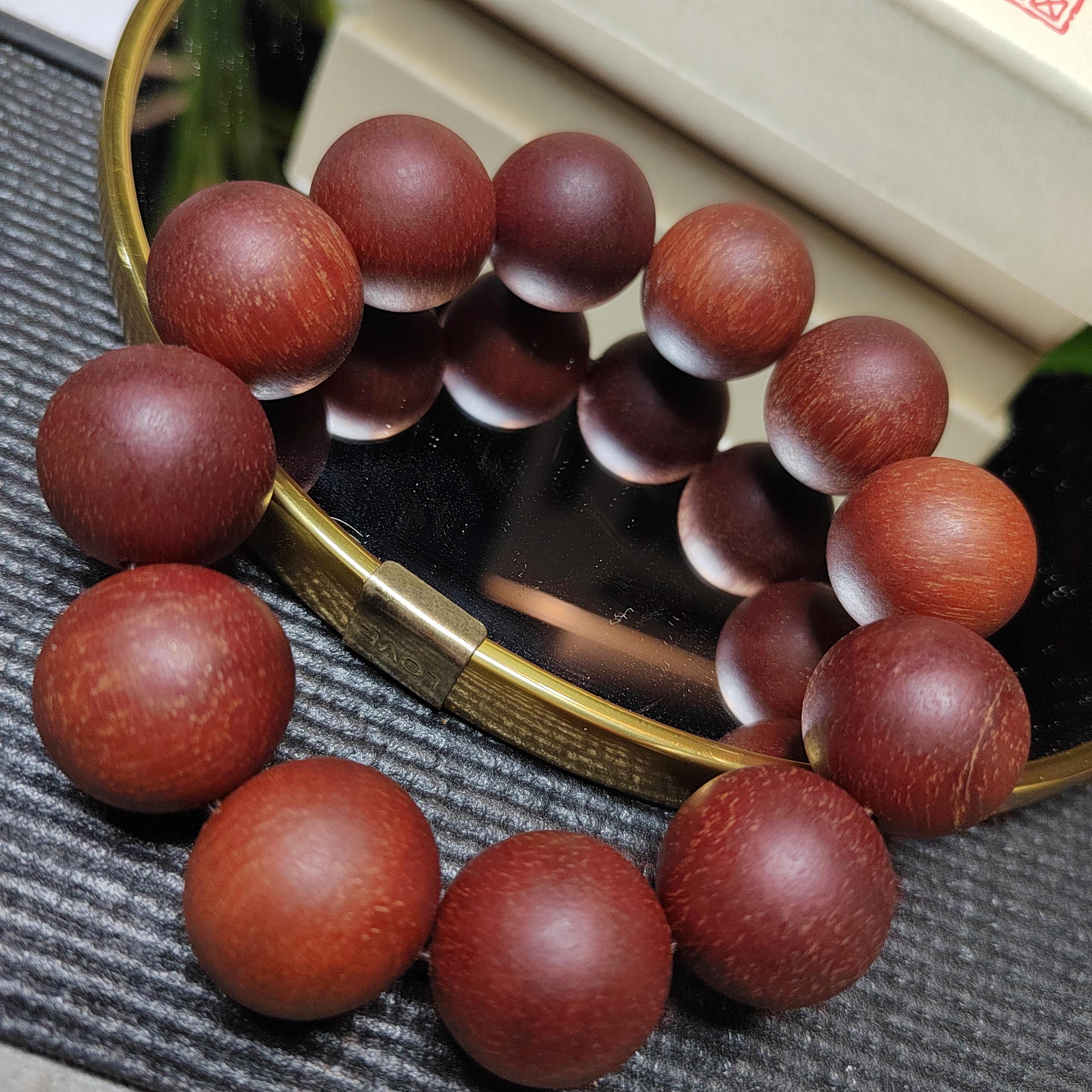 Wooden beaded bracelet on a textured surface with a mirror reflection.