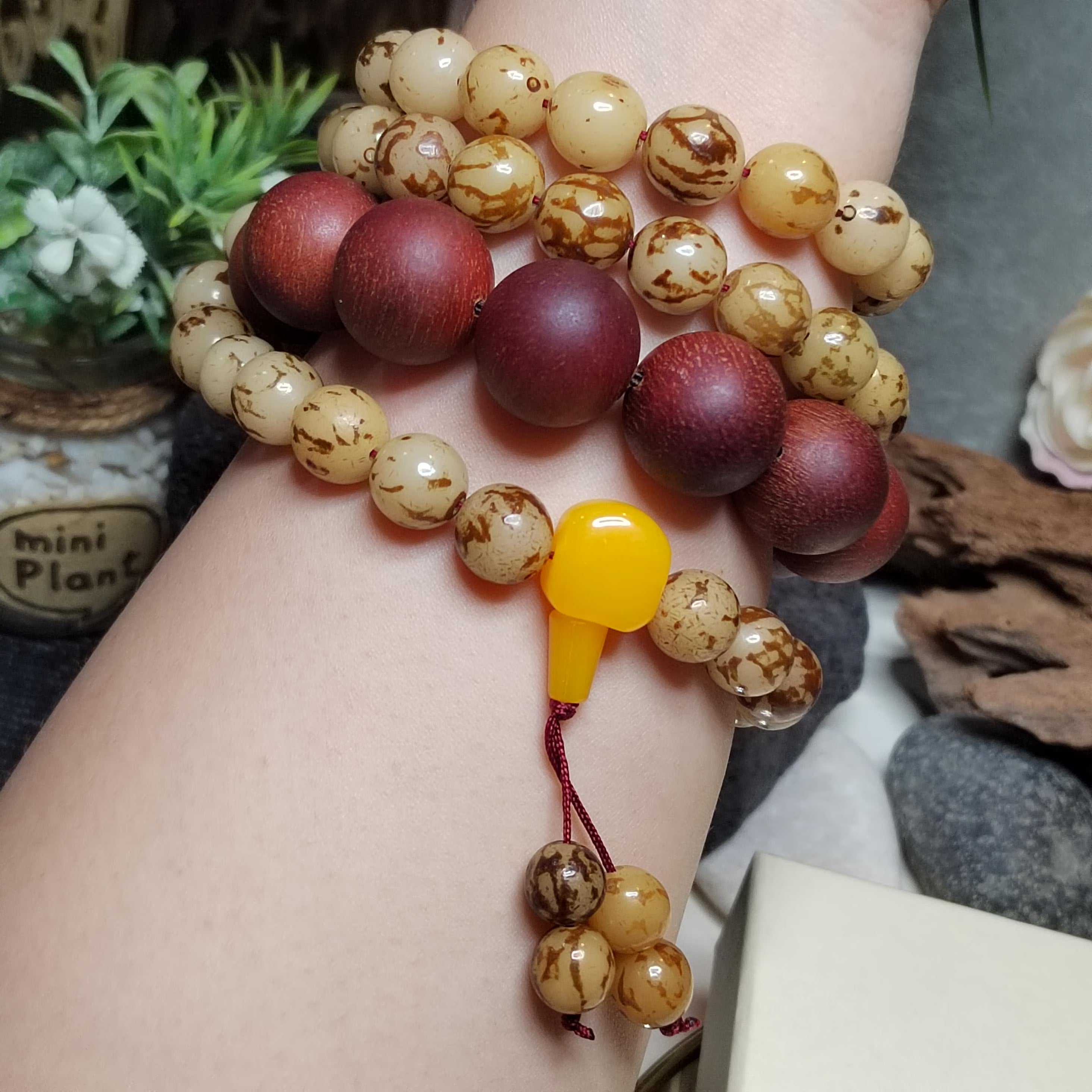 Close-up of a hand wearing a bracelet with maroon, beige, and brown beads.