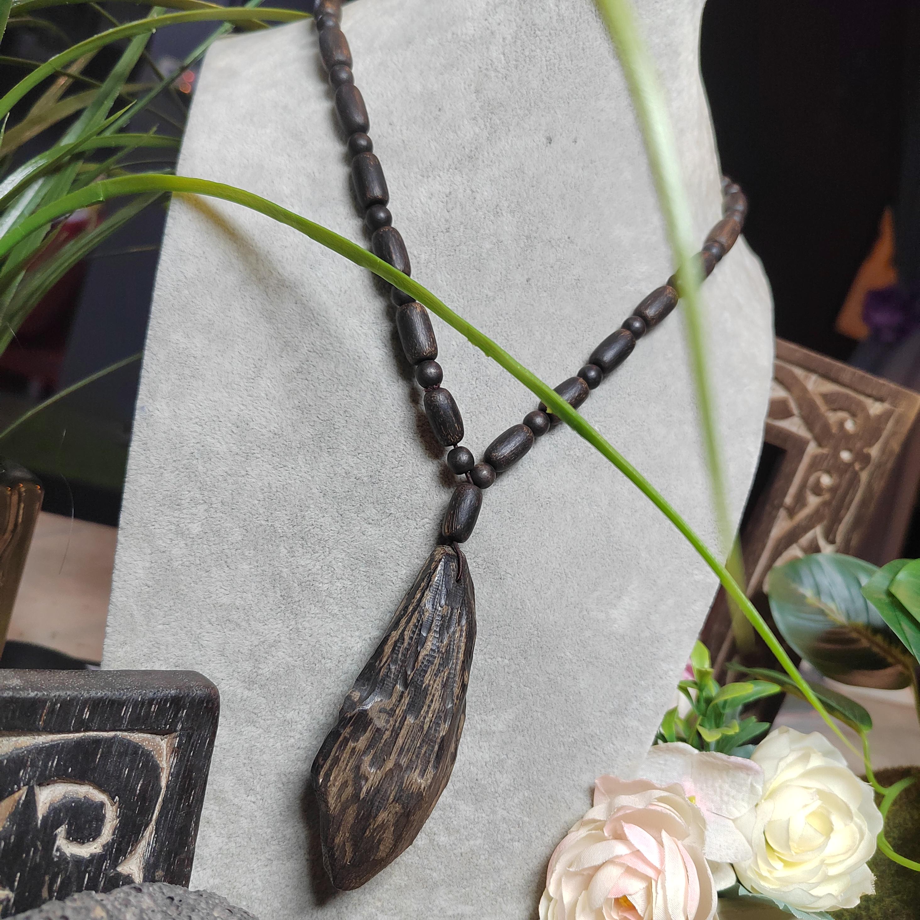 Wooden necklace with leaf-shaped pendant on a stone surface with flowers and plants.