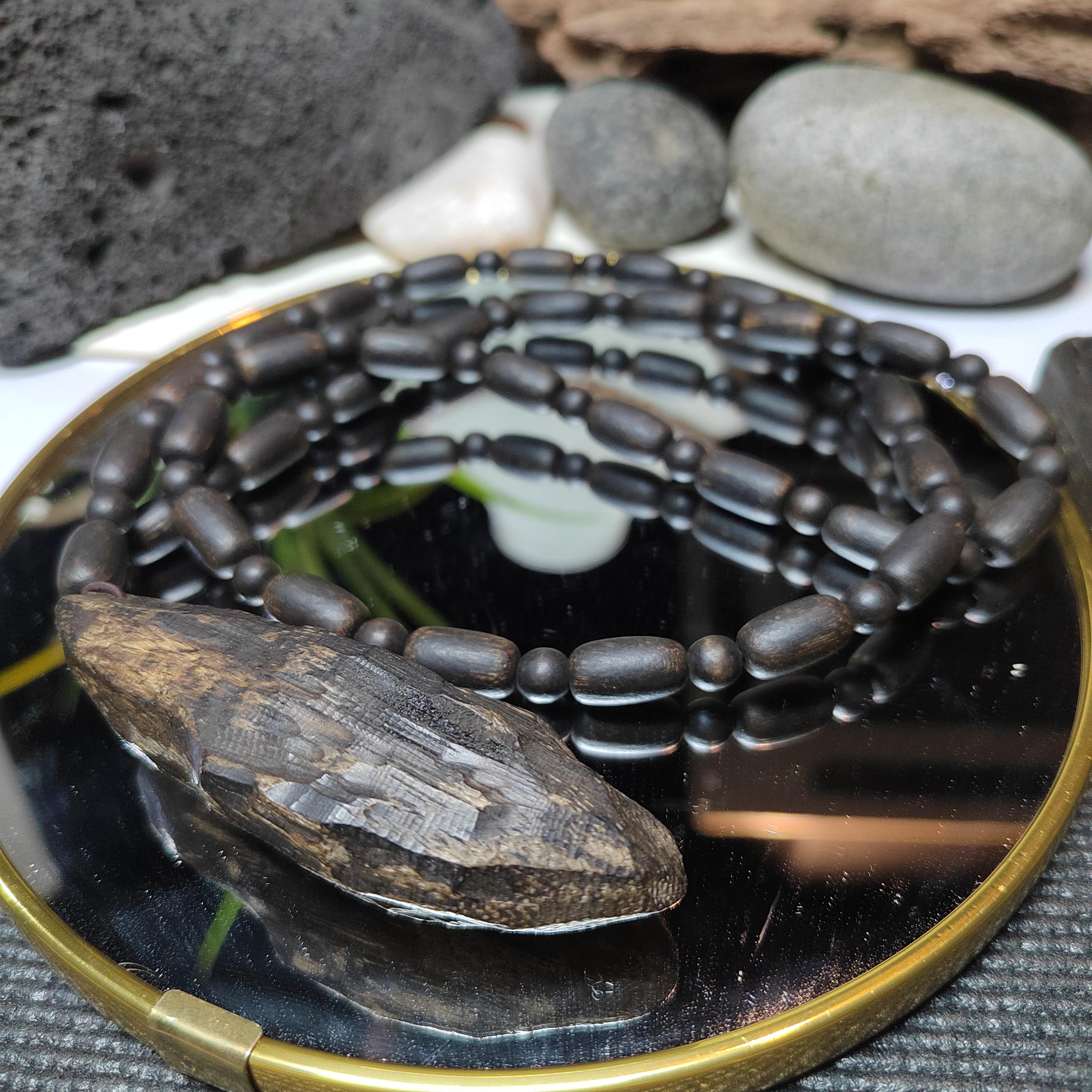 Black beaded necklace with a stone pendant on a reflective surface with stones in the background