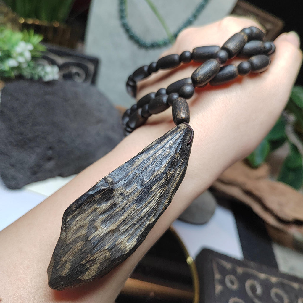 Hand holding a wooden pendant necklace with a blurred natural background
