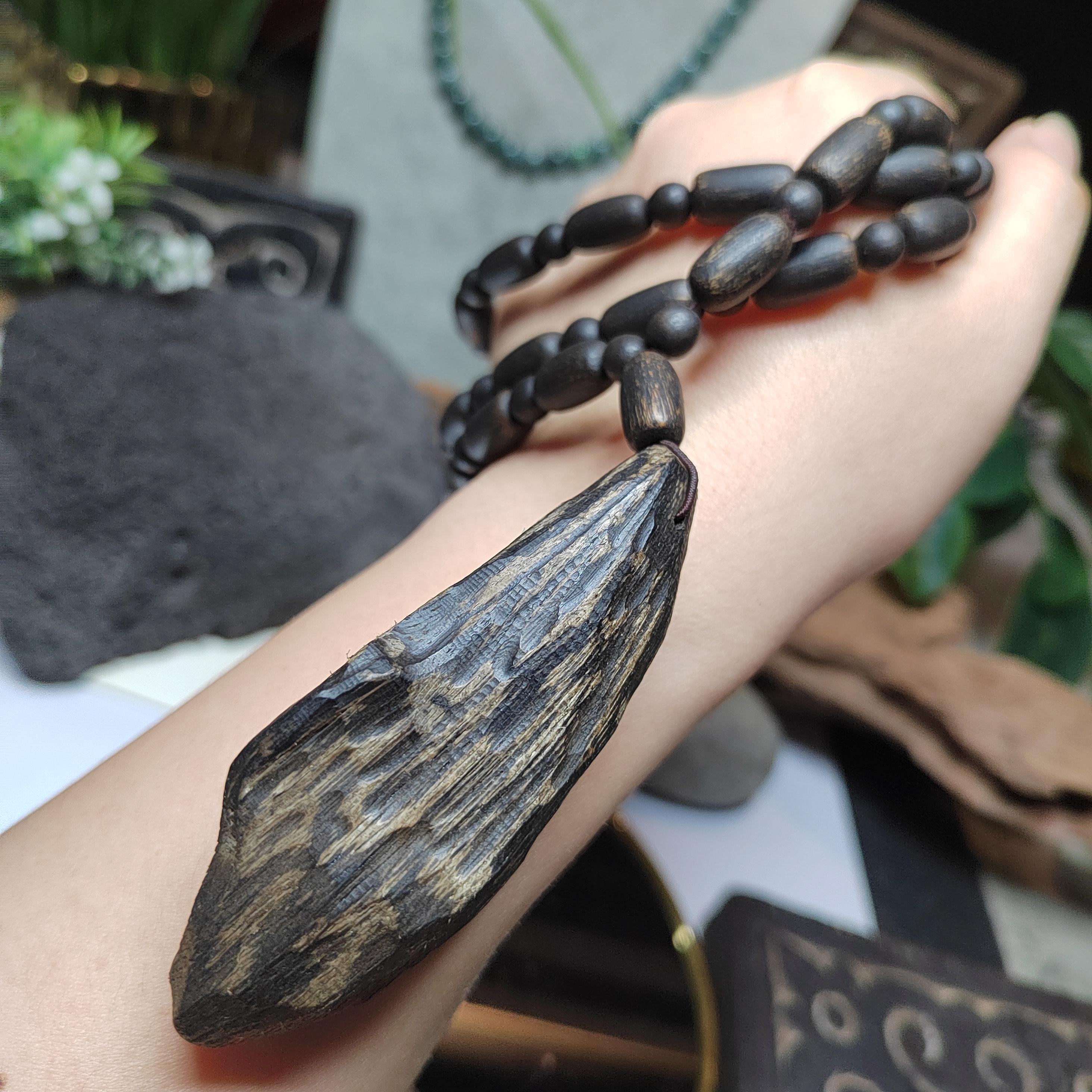 Hand holding a wooden pendant necklace with a blurred natural background