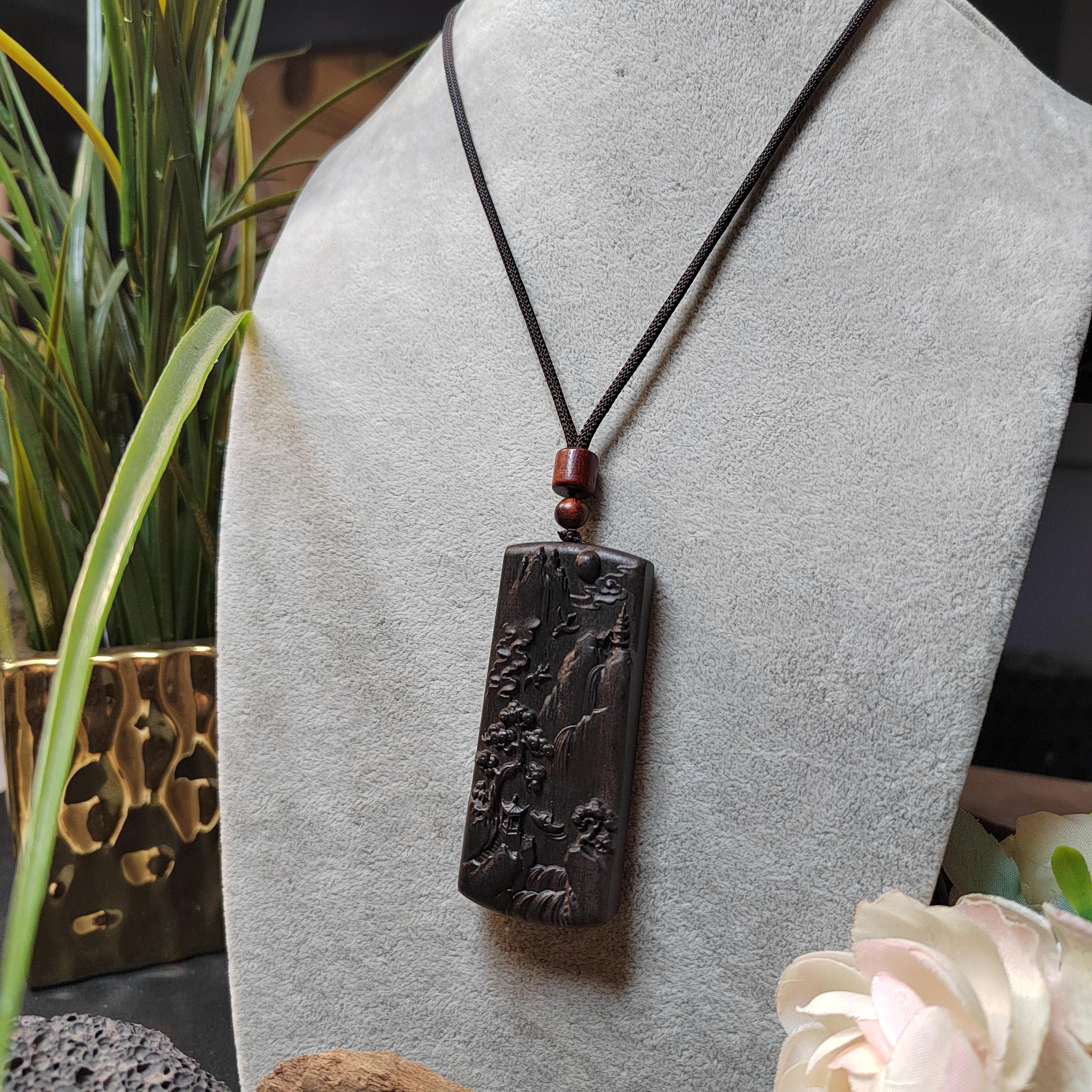 Dark stone pendant necklace on a mannequin bust with plants and flowers in the background