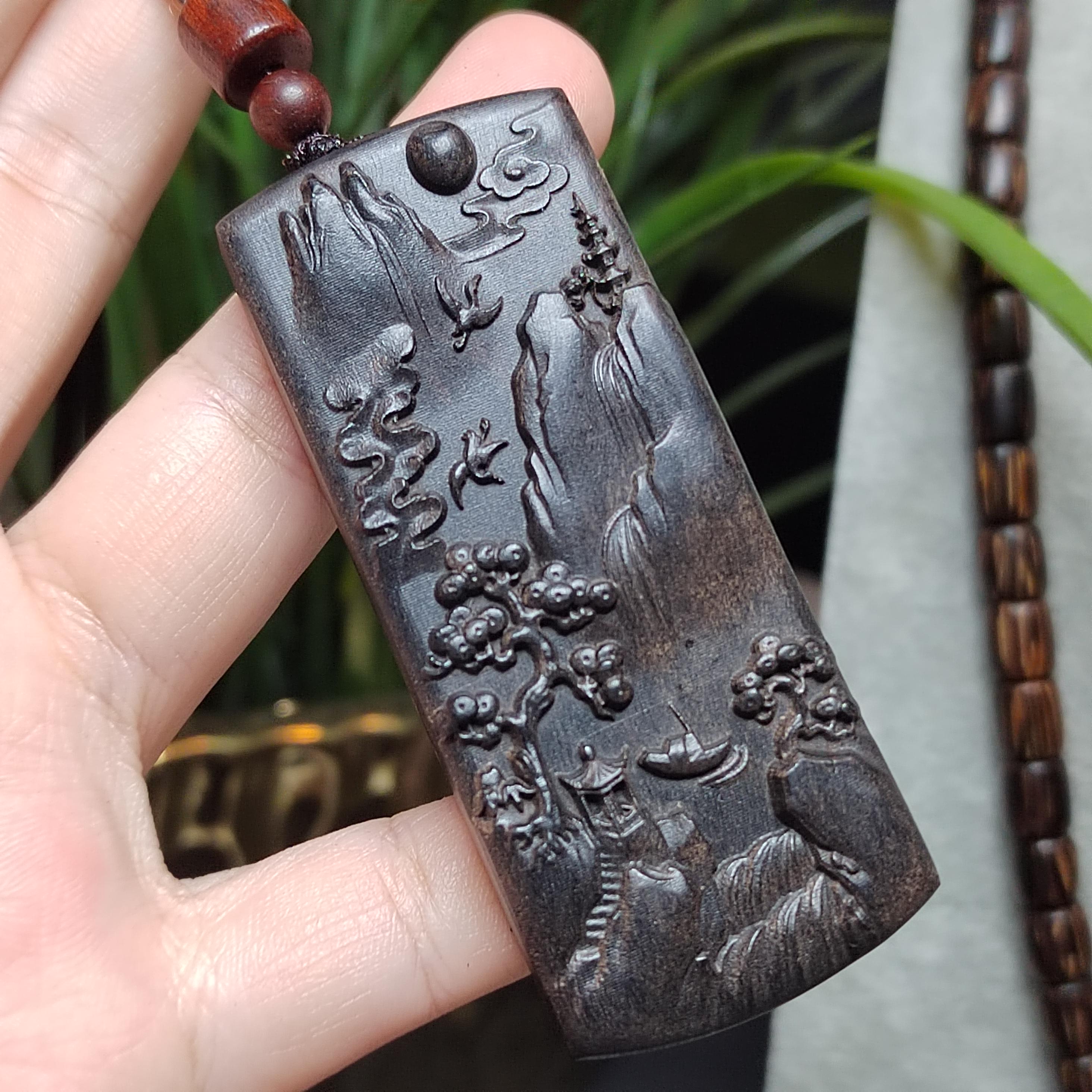 Carved pendant with intricate designs held by a hand against a blurred natural background
