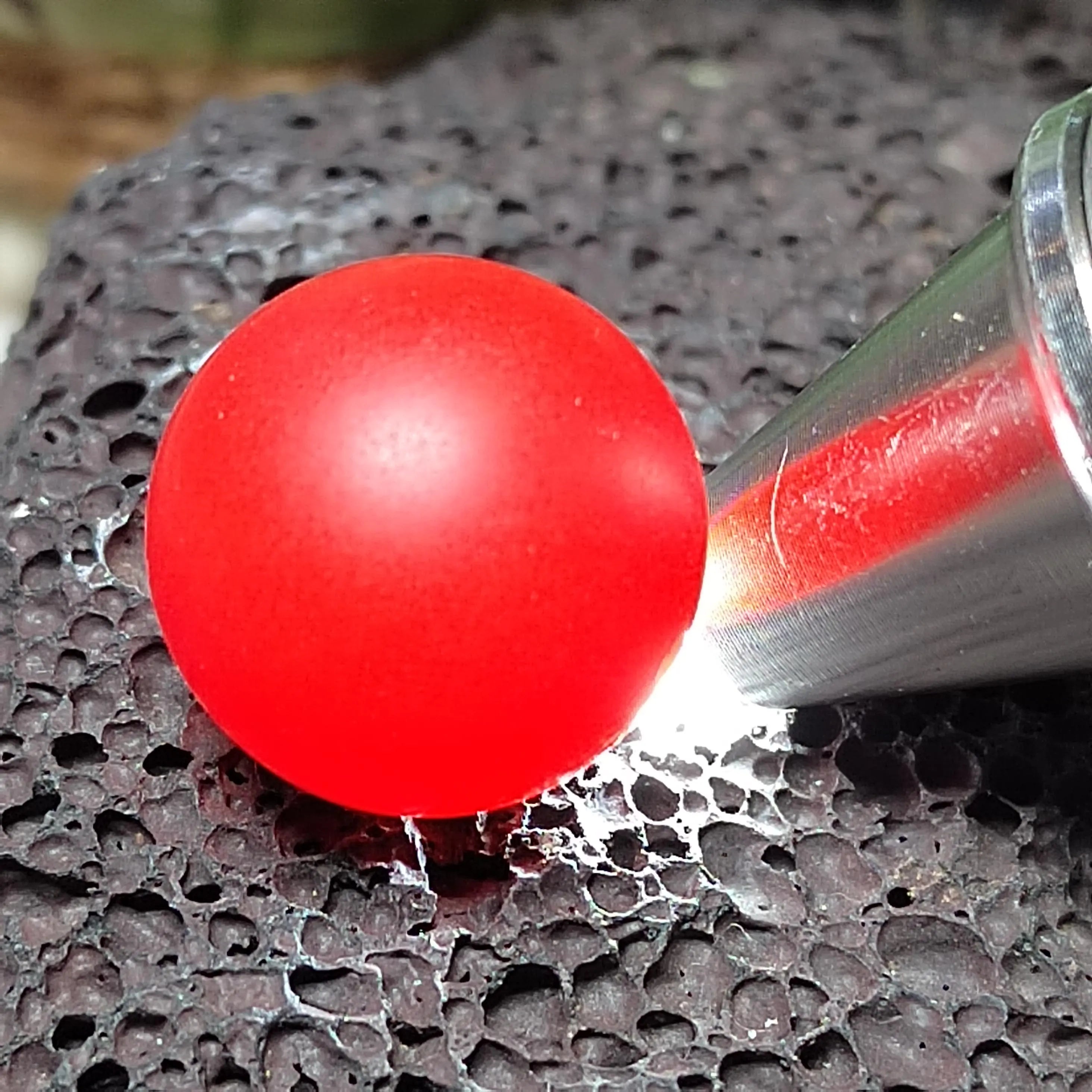 Red Nanhong bead being compressed by a tool on a textured black surface