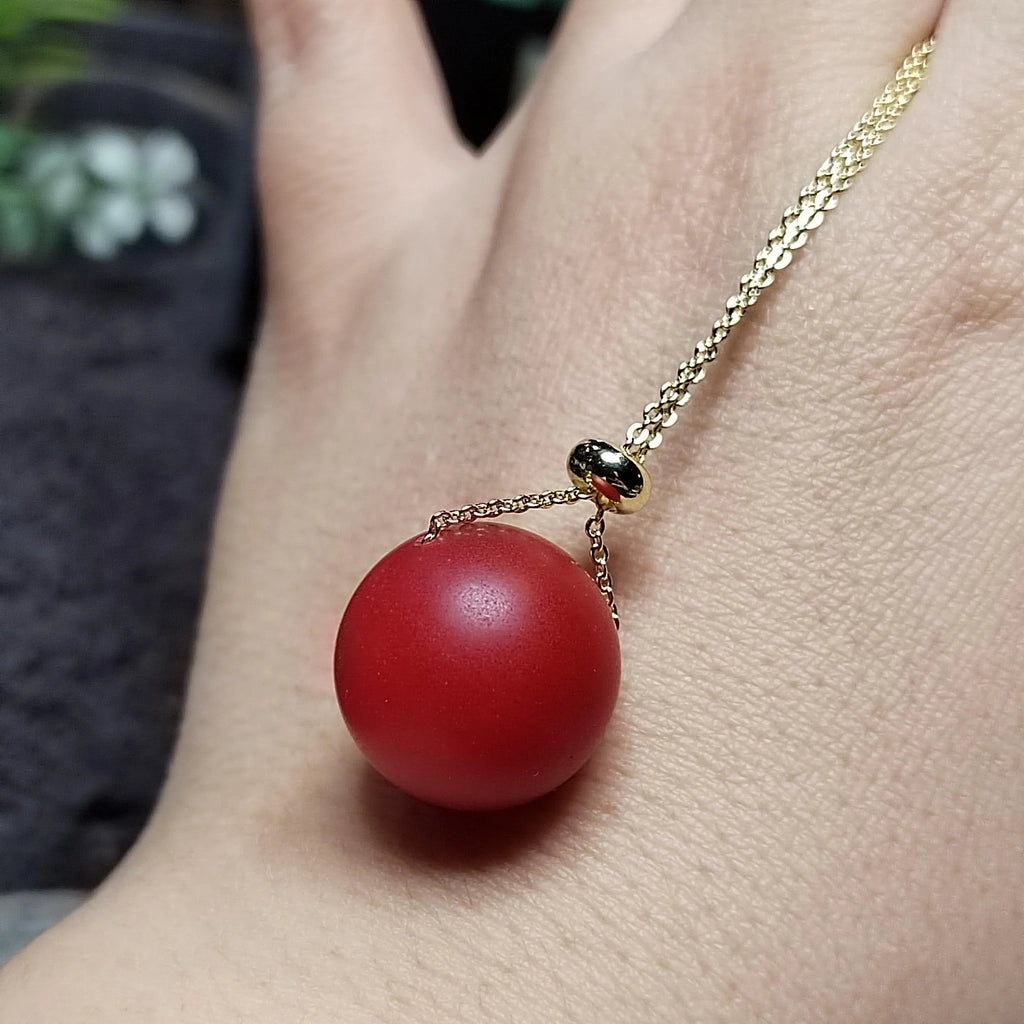 Red sphere pendant on a gold chain against a blurred background