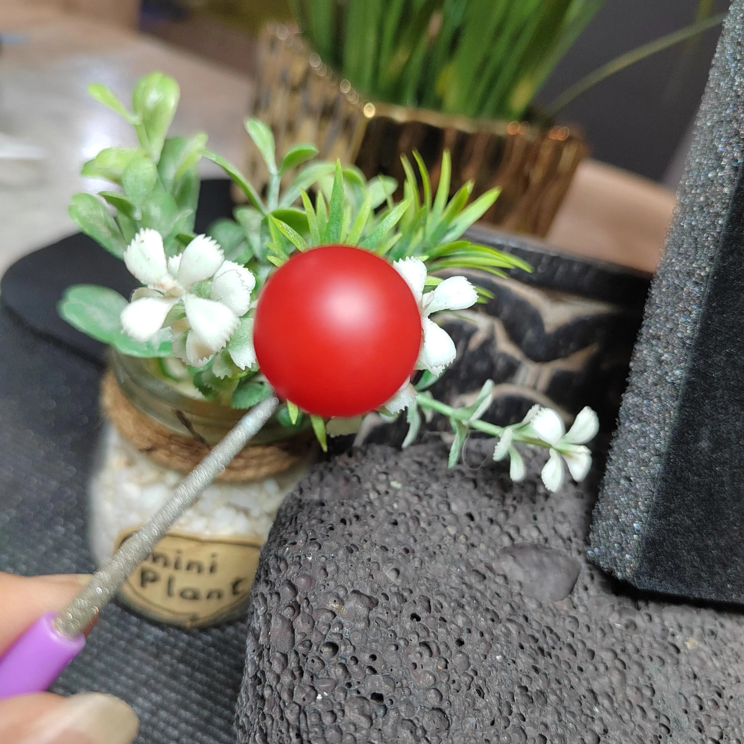 Decorative item with red ball and greenery on a textured surface