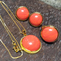 Jewelry set with coral-colored stones and gold accents on a dark surface