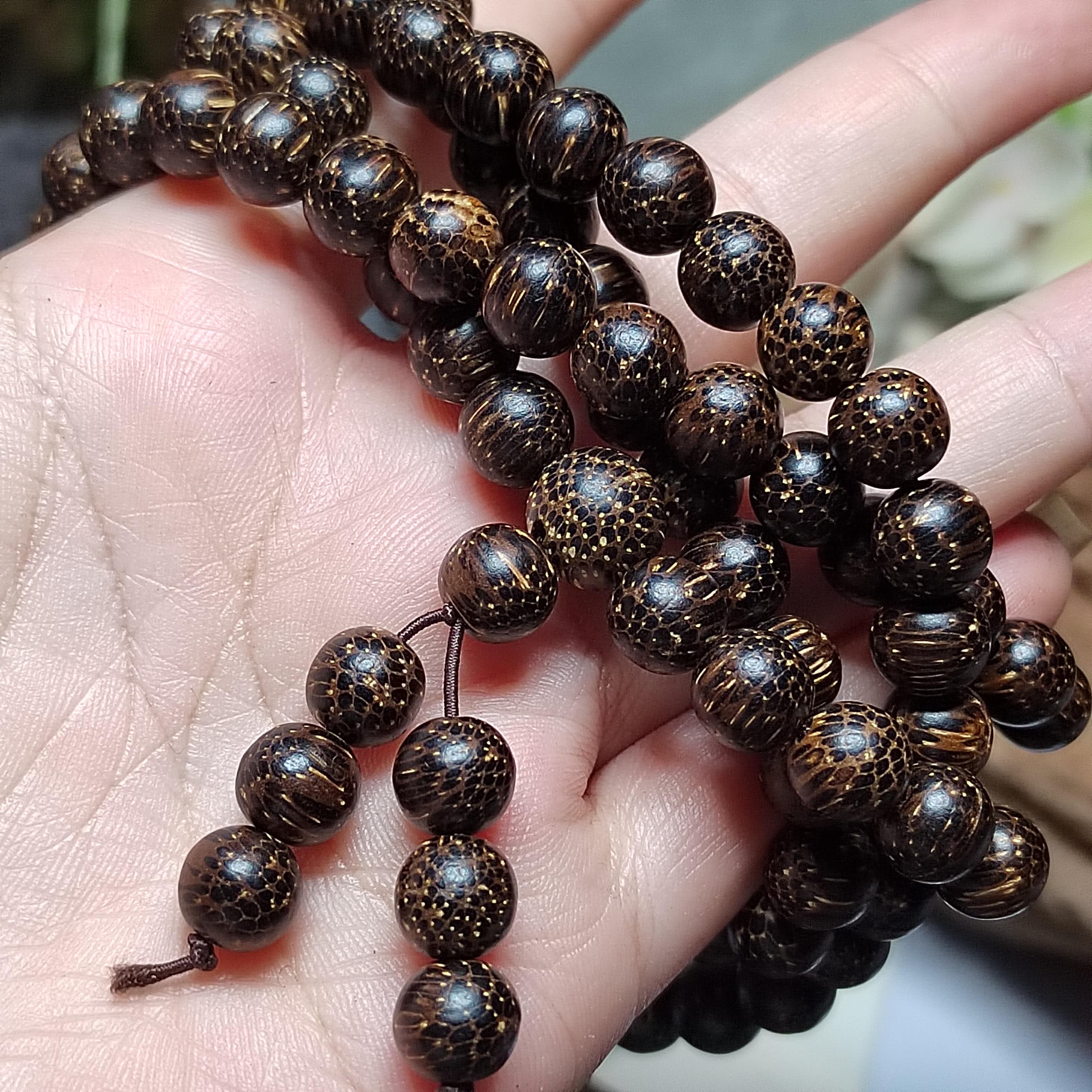 Close-up of a hand holding a string of dark brown beaded rosary.