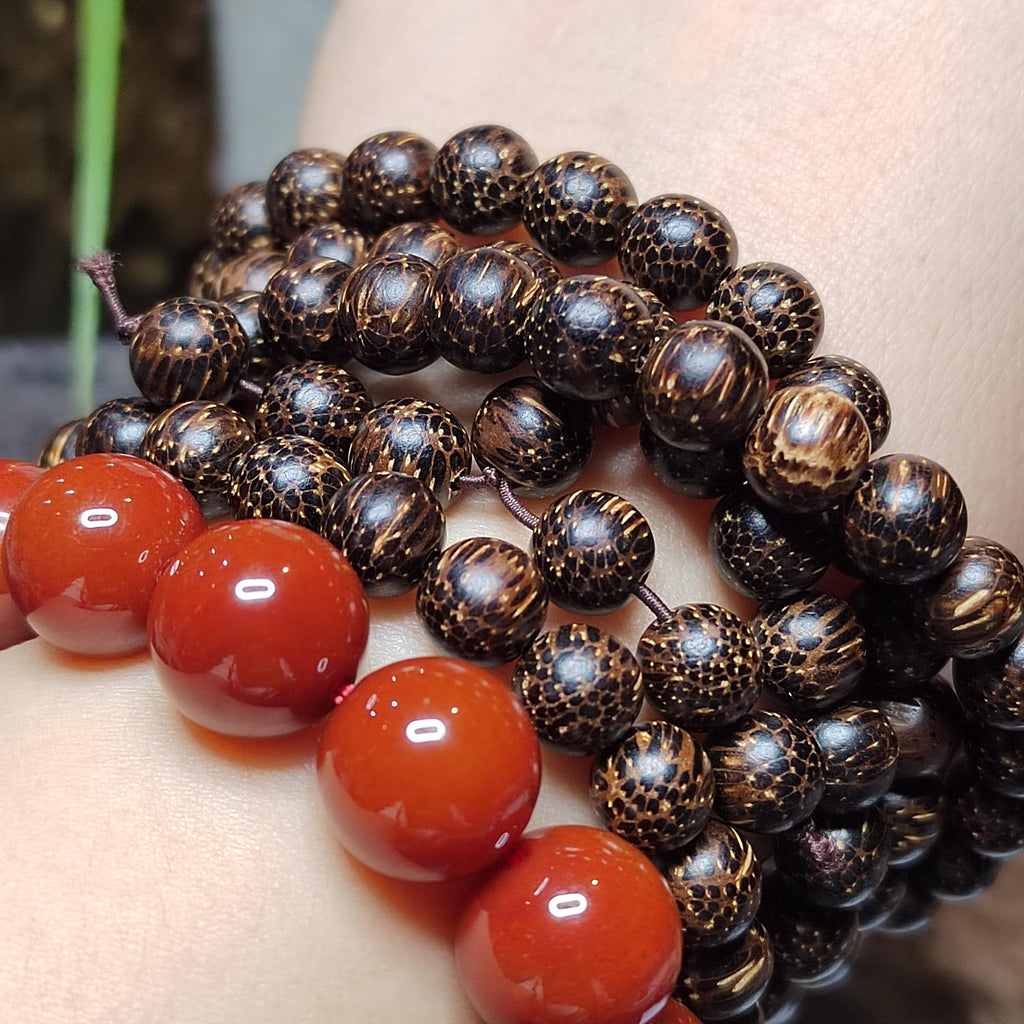 Close-up of a bracelet with dark brown beads and red stones on a person's wrist.