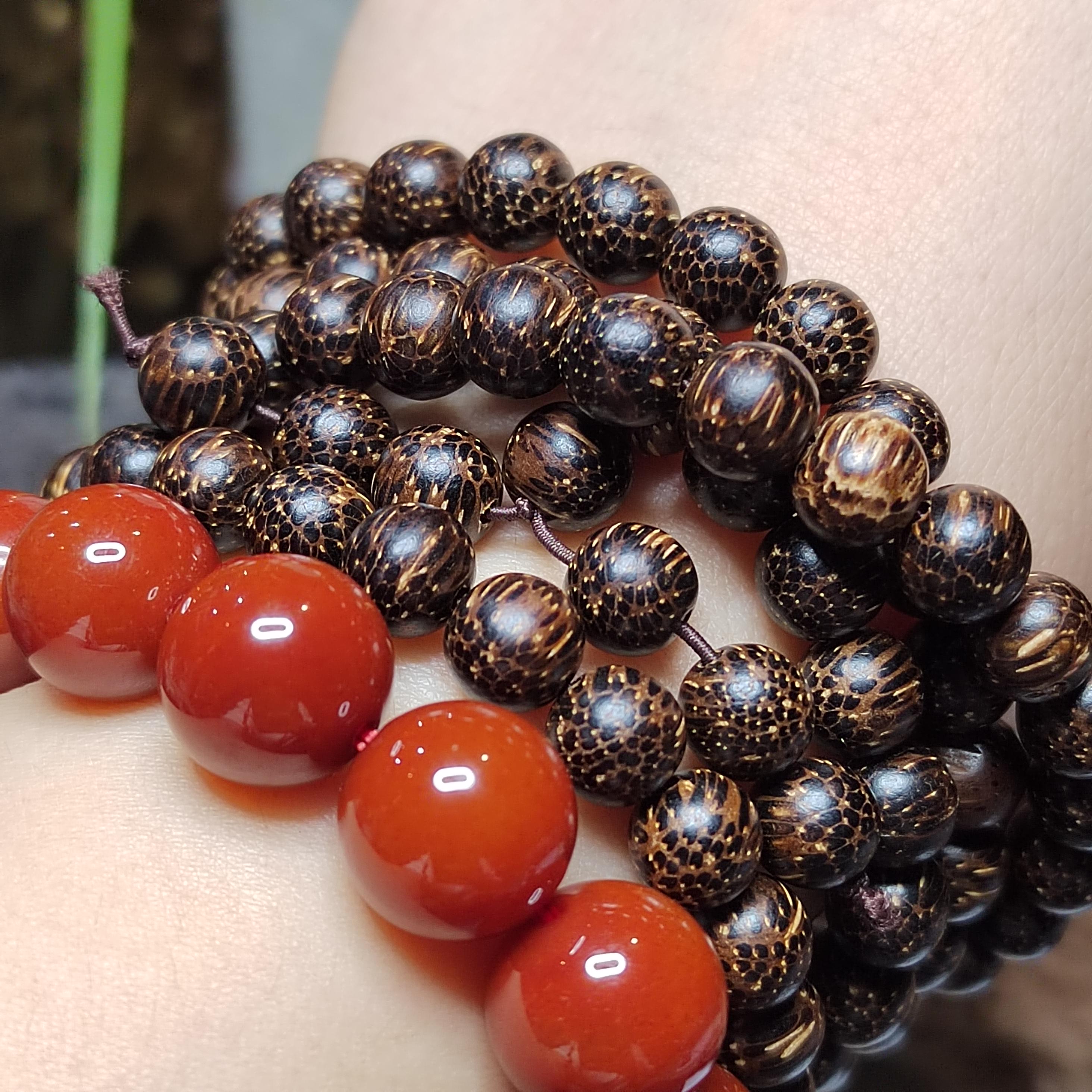 Close-up of a bracelet with dark brown beads and red stones on a person's wrist.